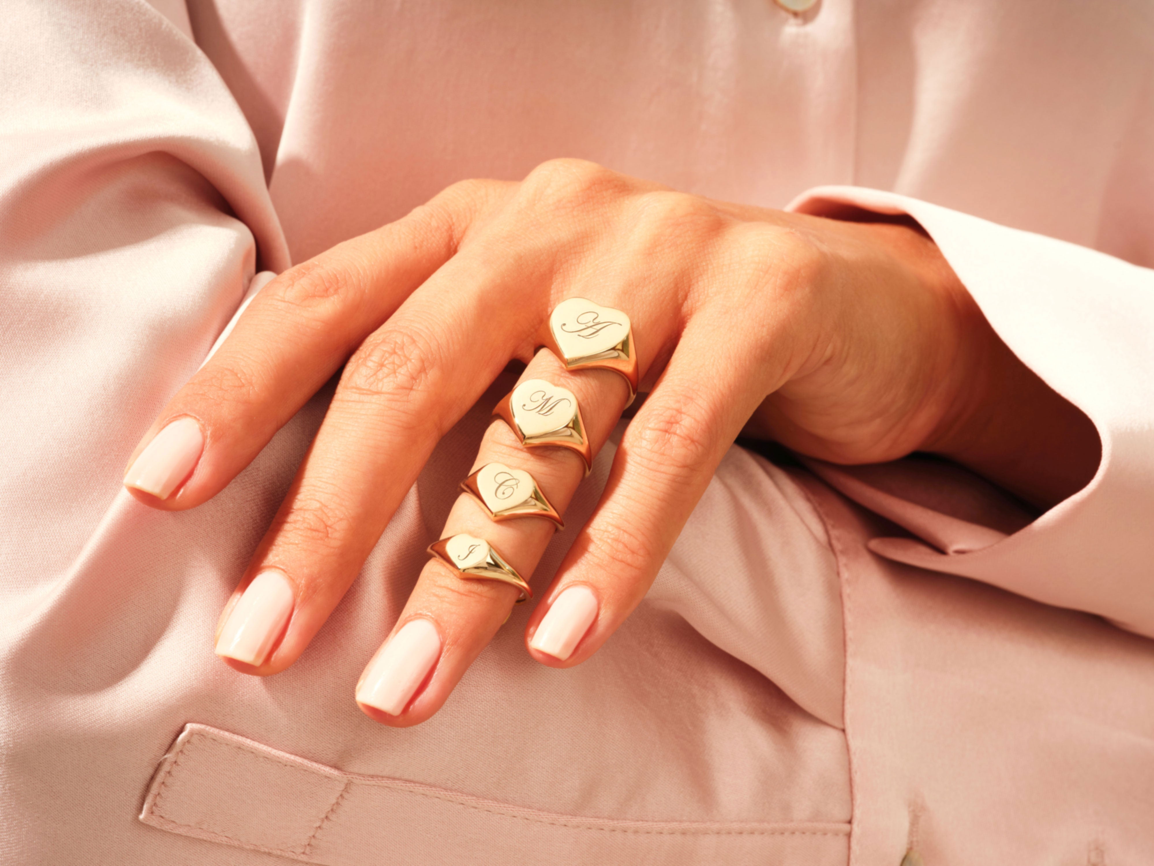Gold heart signet rings with engraved initials on a hand
