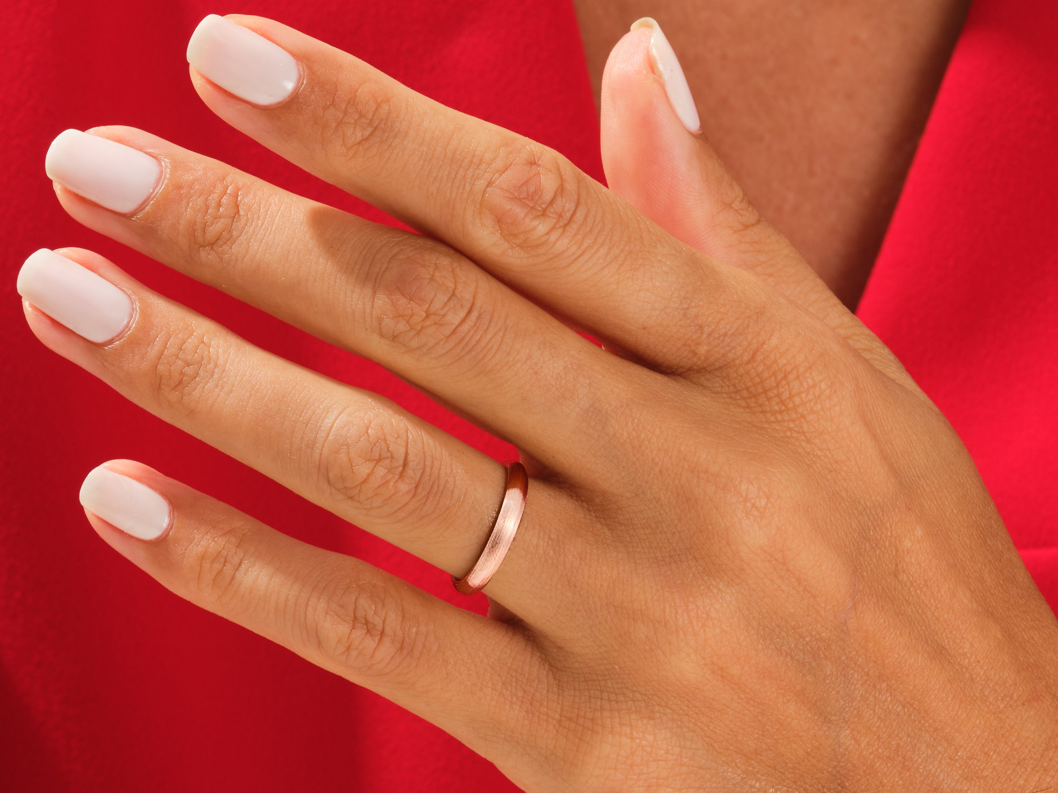 Rose gold wedding band on a hand with white nails