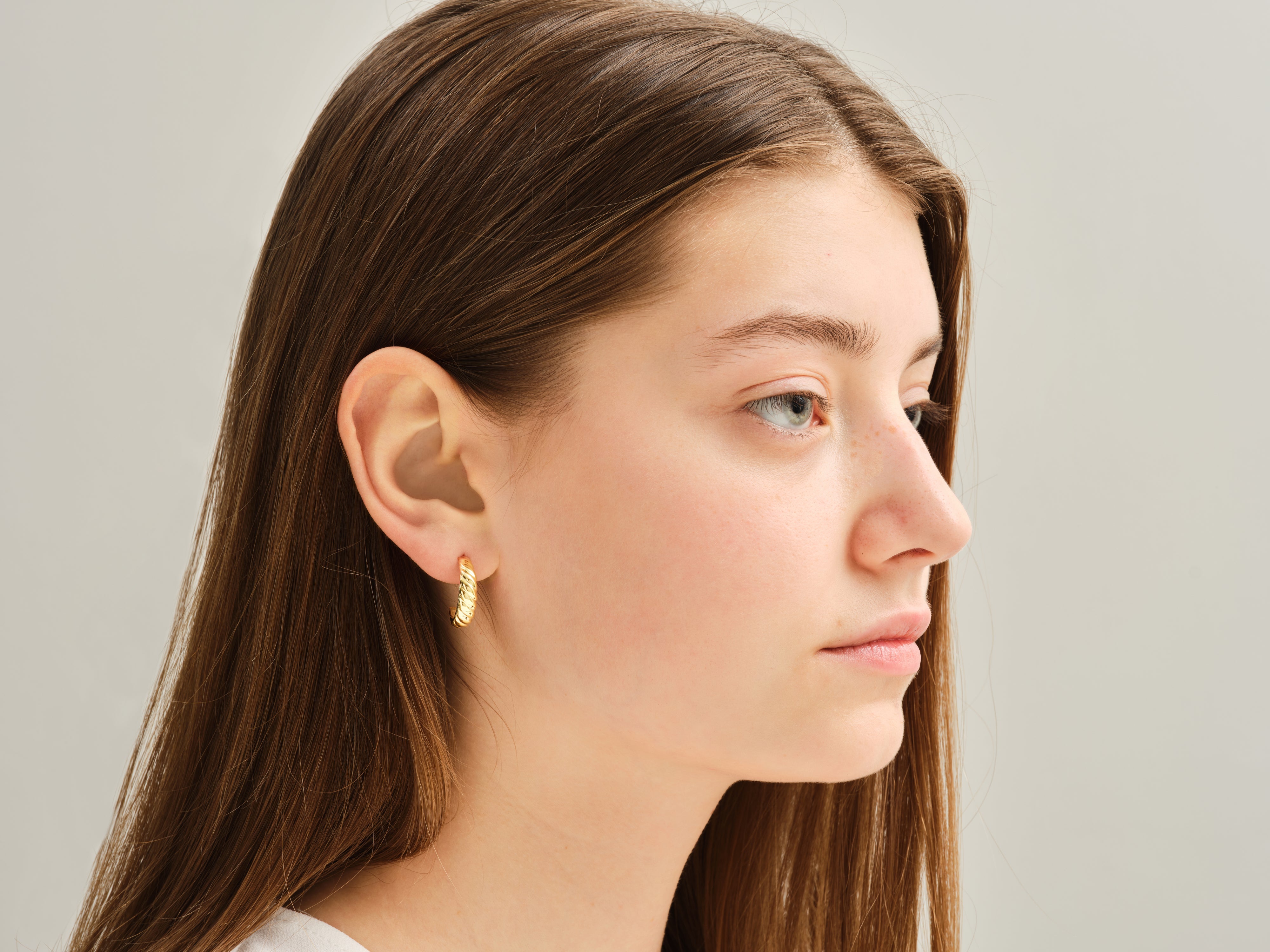 Gold twisted hoop earring on a woman's ear, jewelry