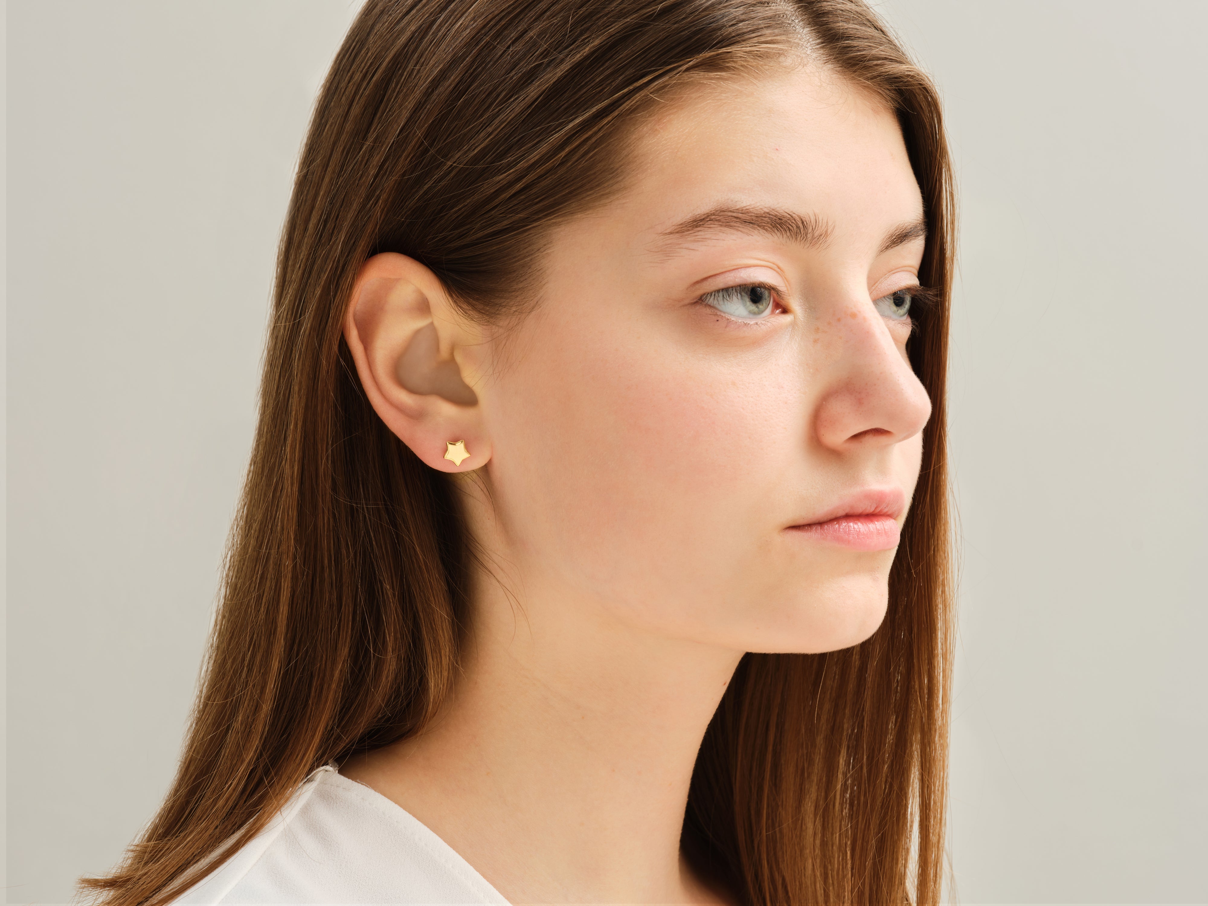 Gold star stud earrings on a young woman's ear