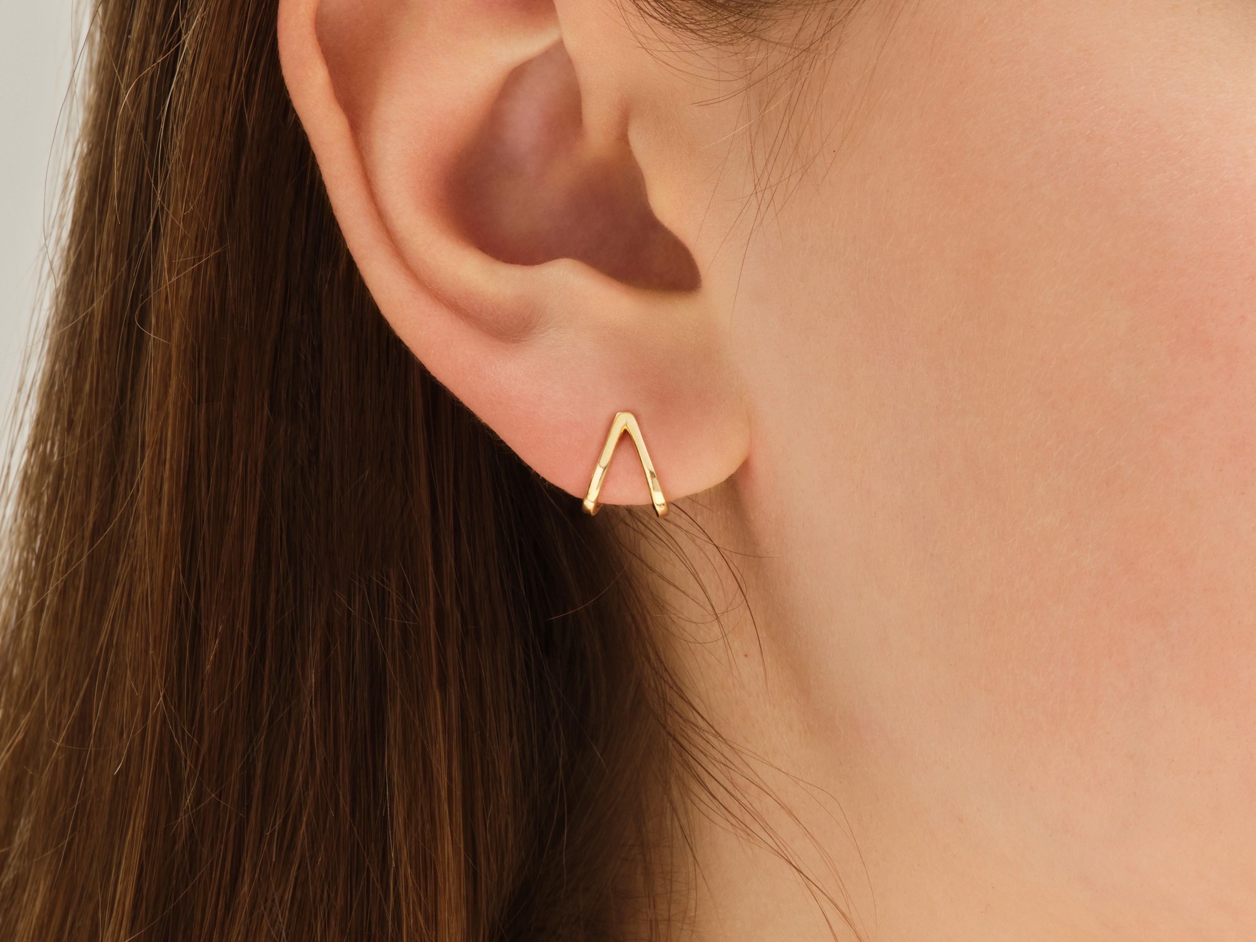 Gold V-shaped stud earring on a woman's ear
