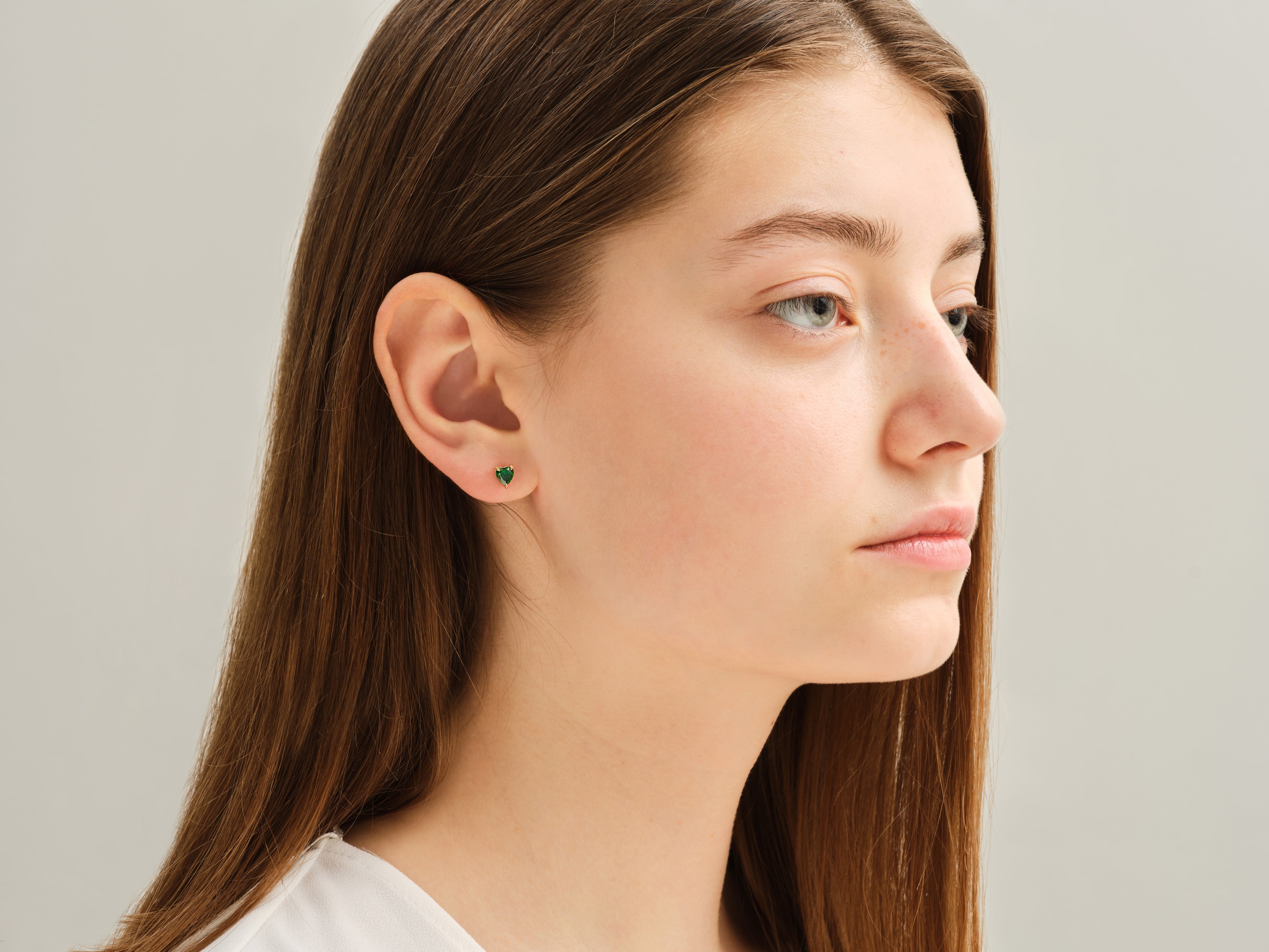 Heart-shaped emerald stud earrings on a model's ear
