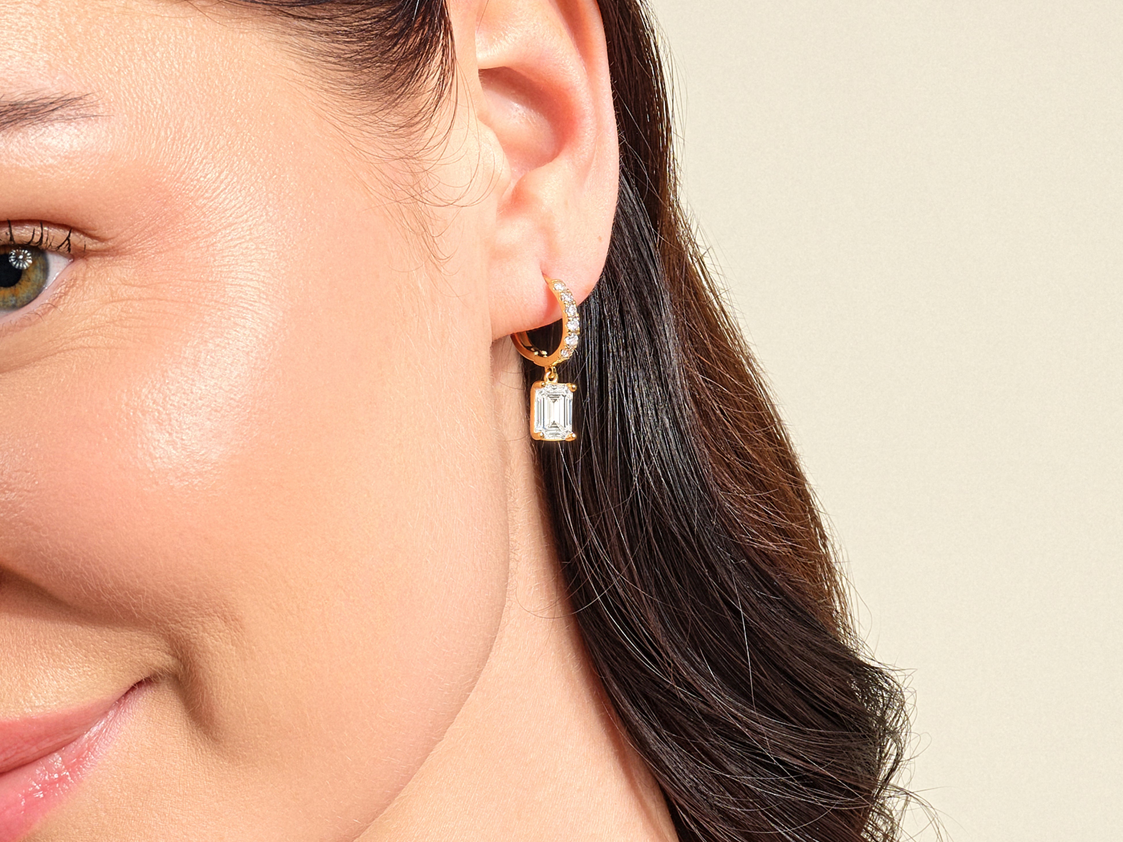 Gold emerald cut diamond dangle earrings on model