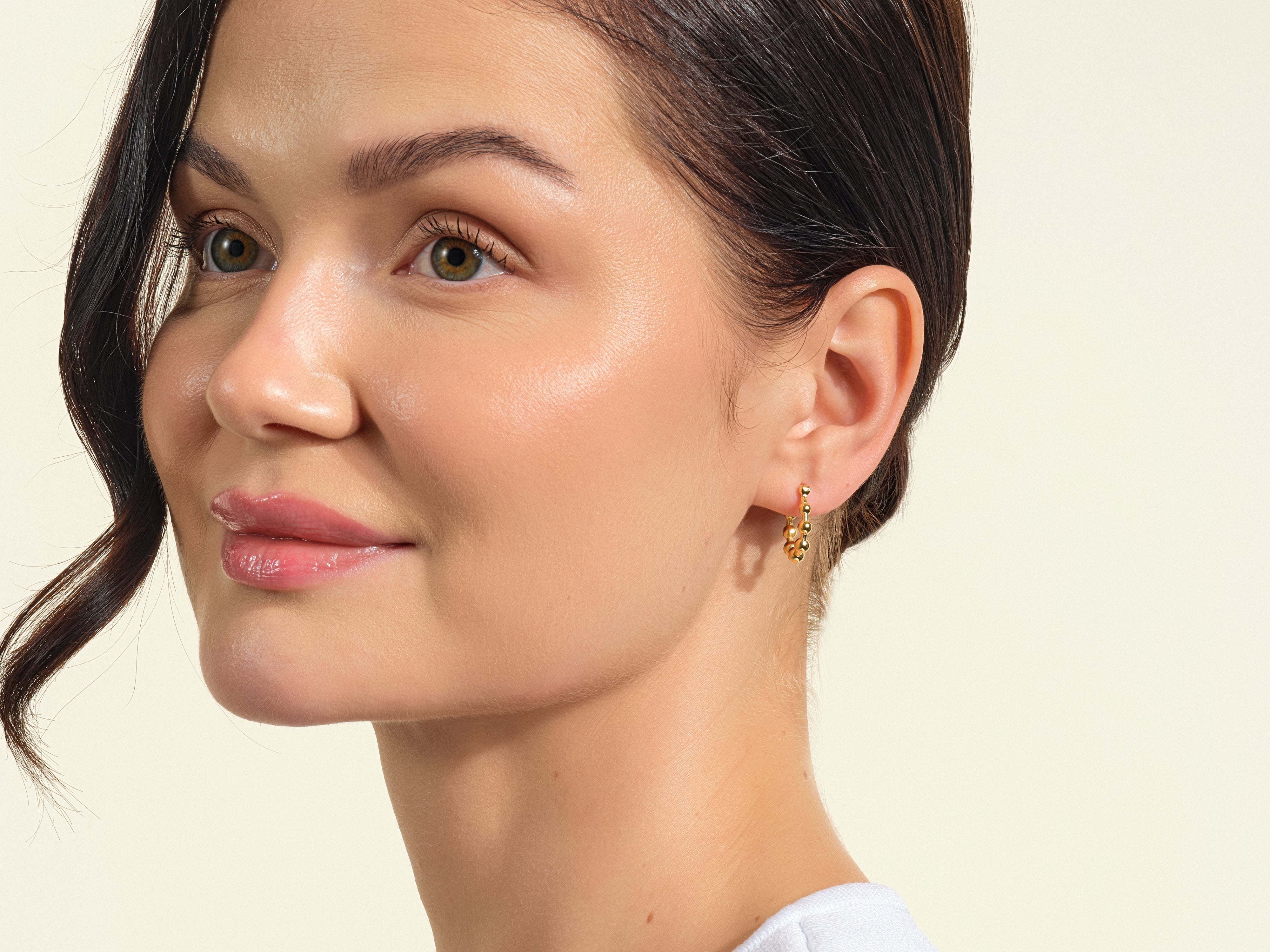 Gold beaded hoop earrings on a woman's ear, jewelry