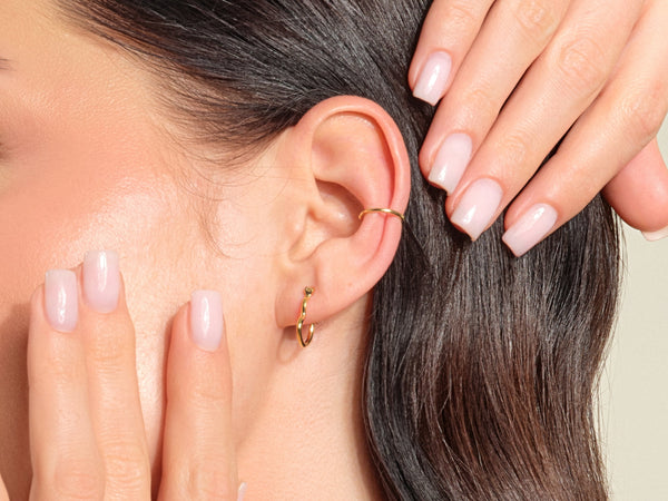 Gold ear cuff and hoop earrings on a woman's ear
