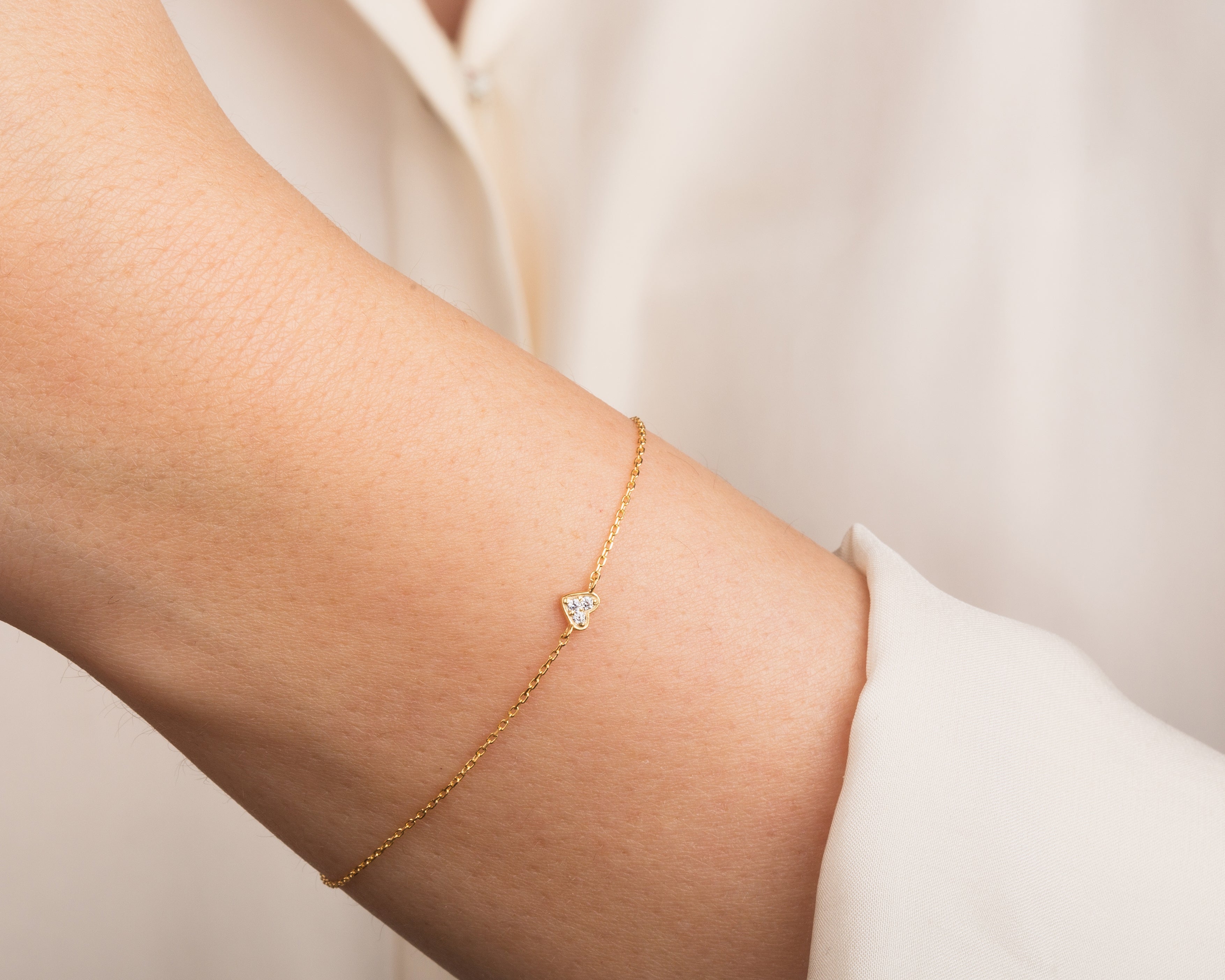Gold bracelet with diamond heart charm on wrist