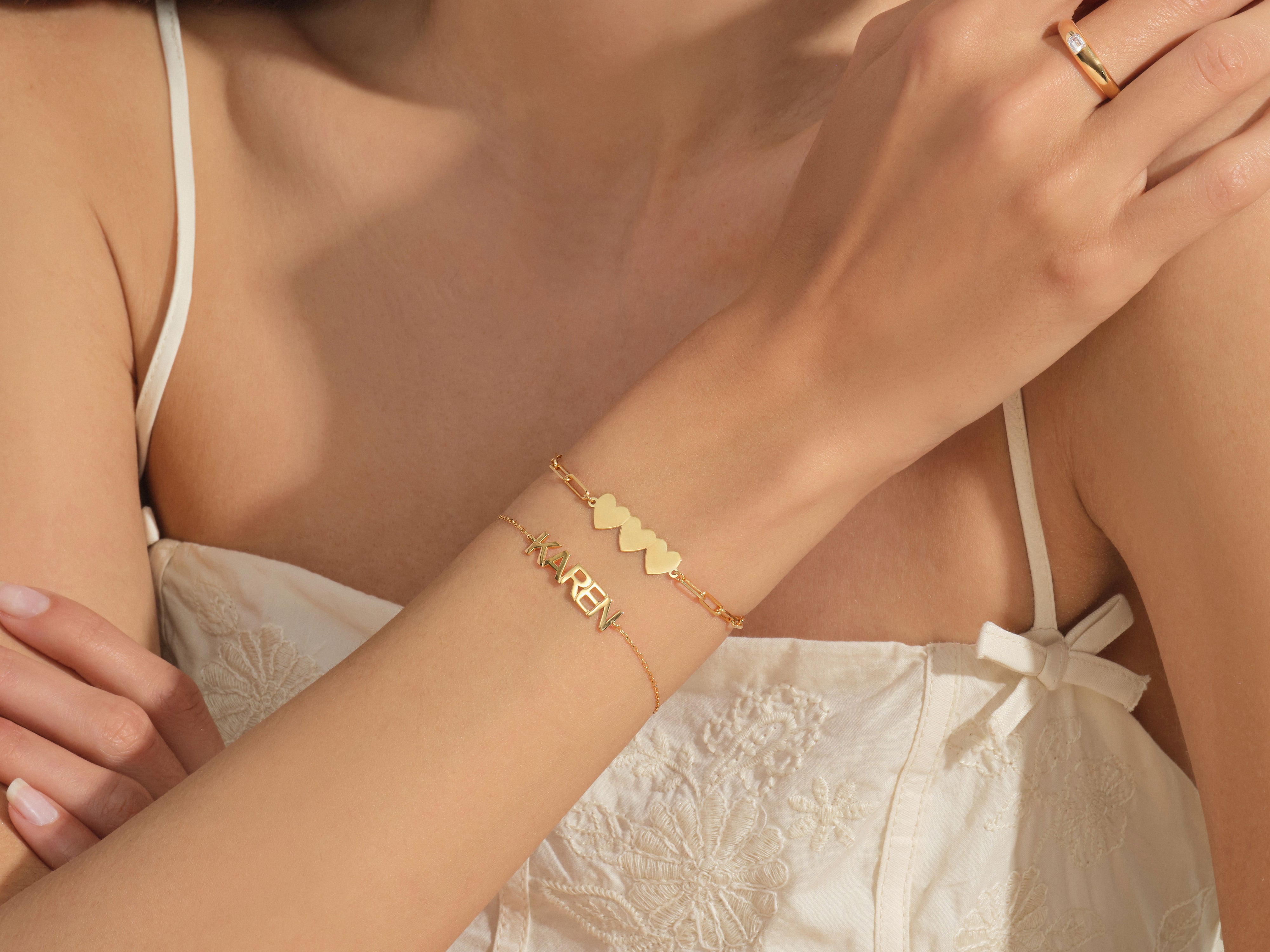 Gold name bracelet and heart charm bracelet on arm