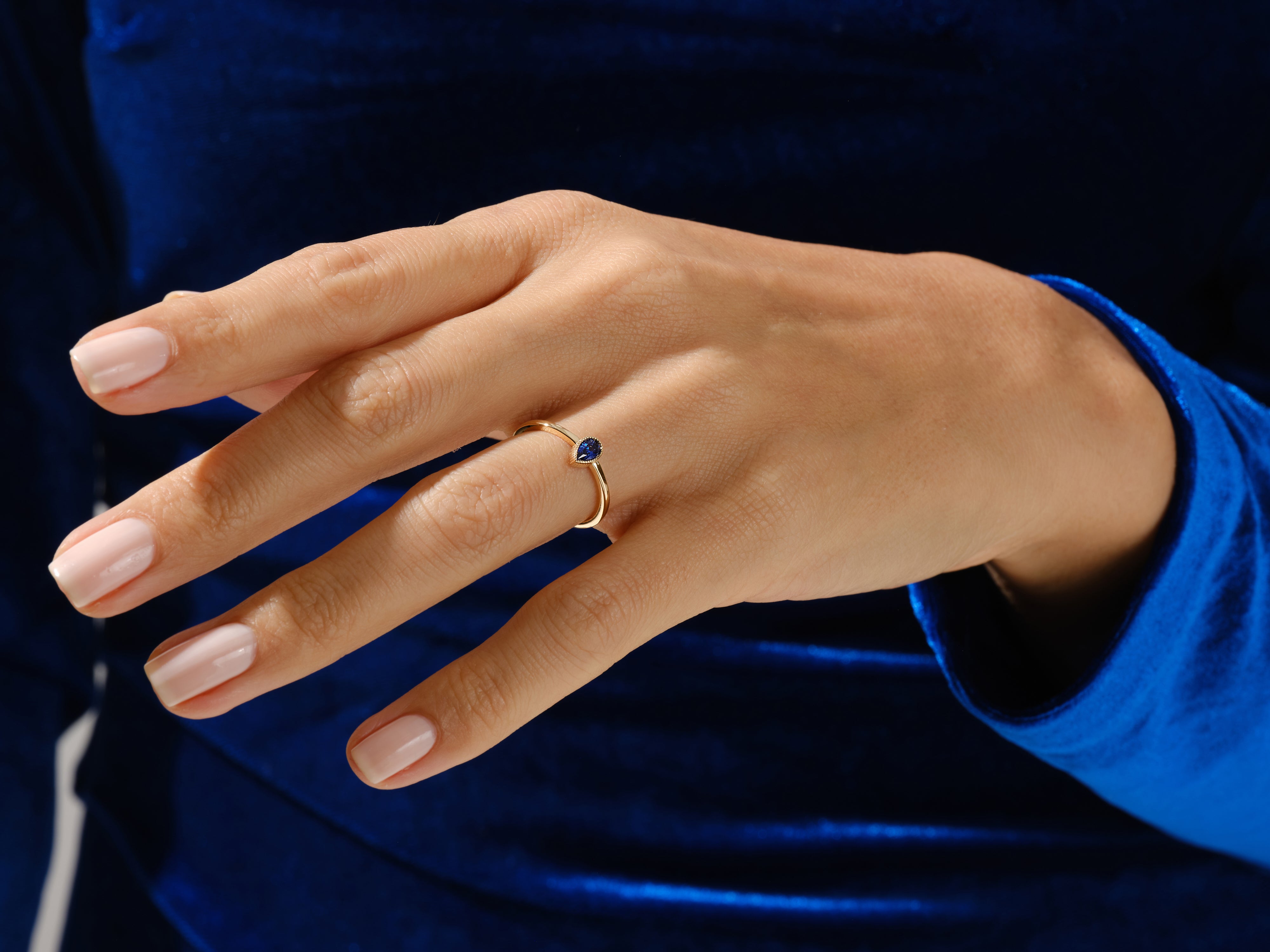 Gold ring with pear-shaped sapphire on a hand