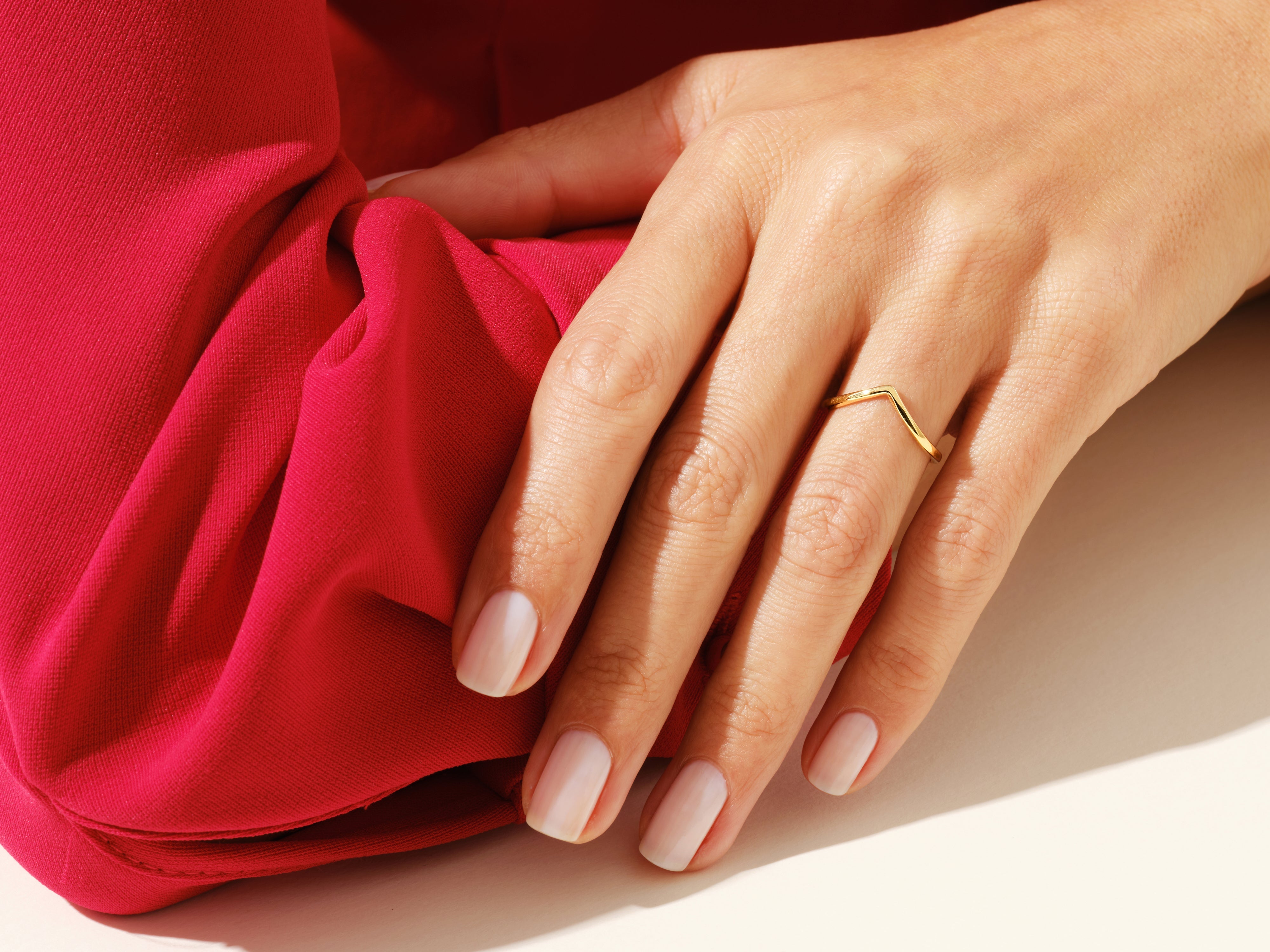 Gold chevron ring on hand against red fabric, jewelry photography