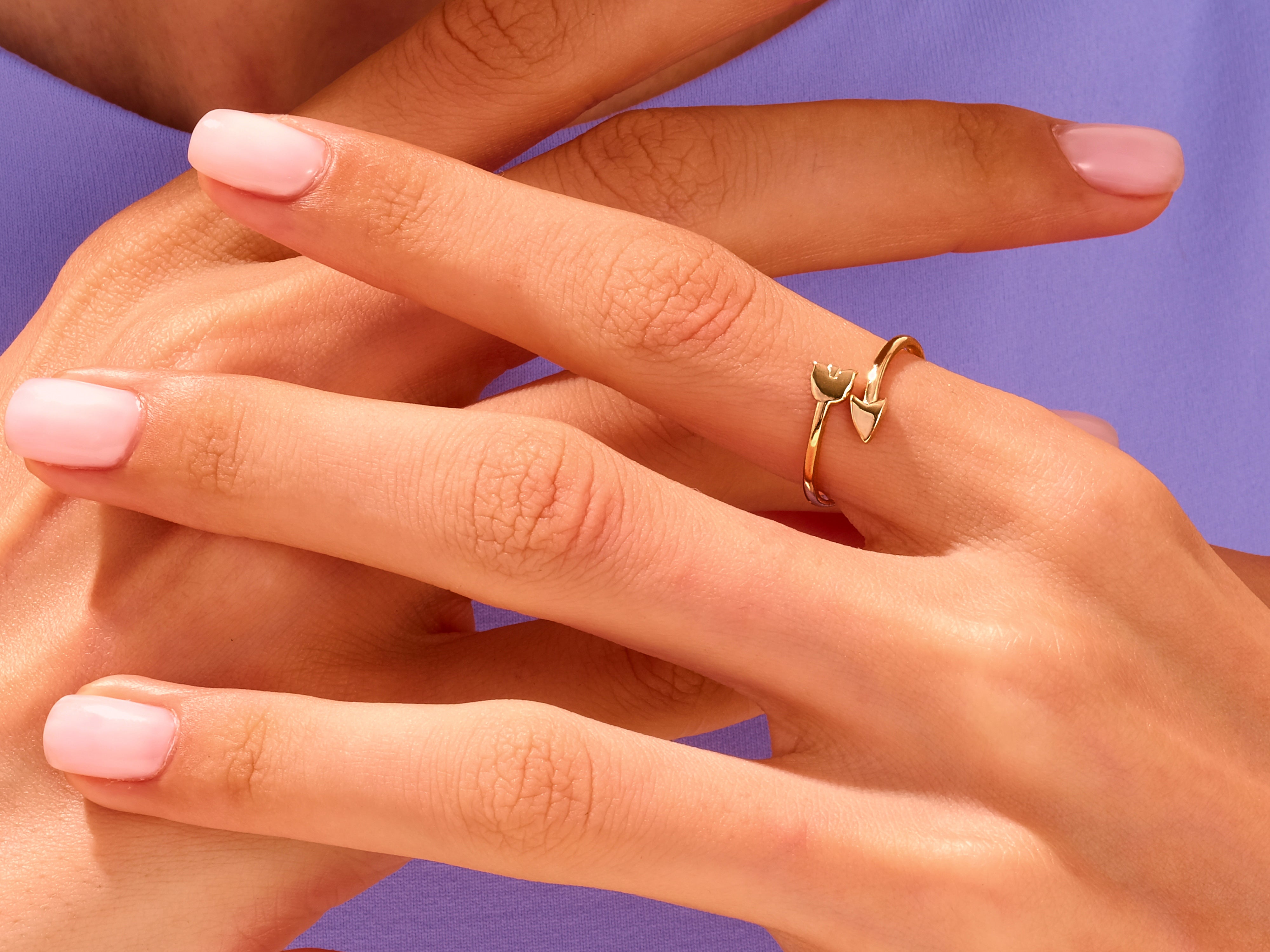 Gold tulip and arrow ring on a hand with pink nails