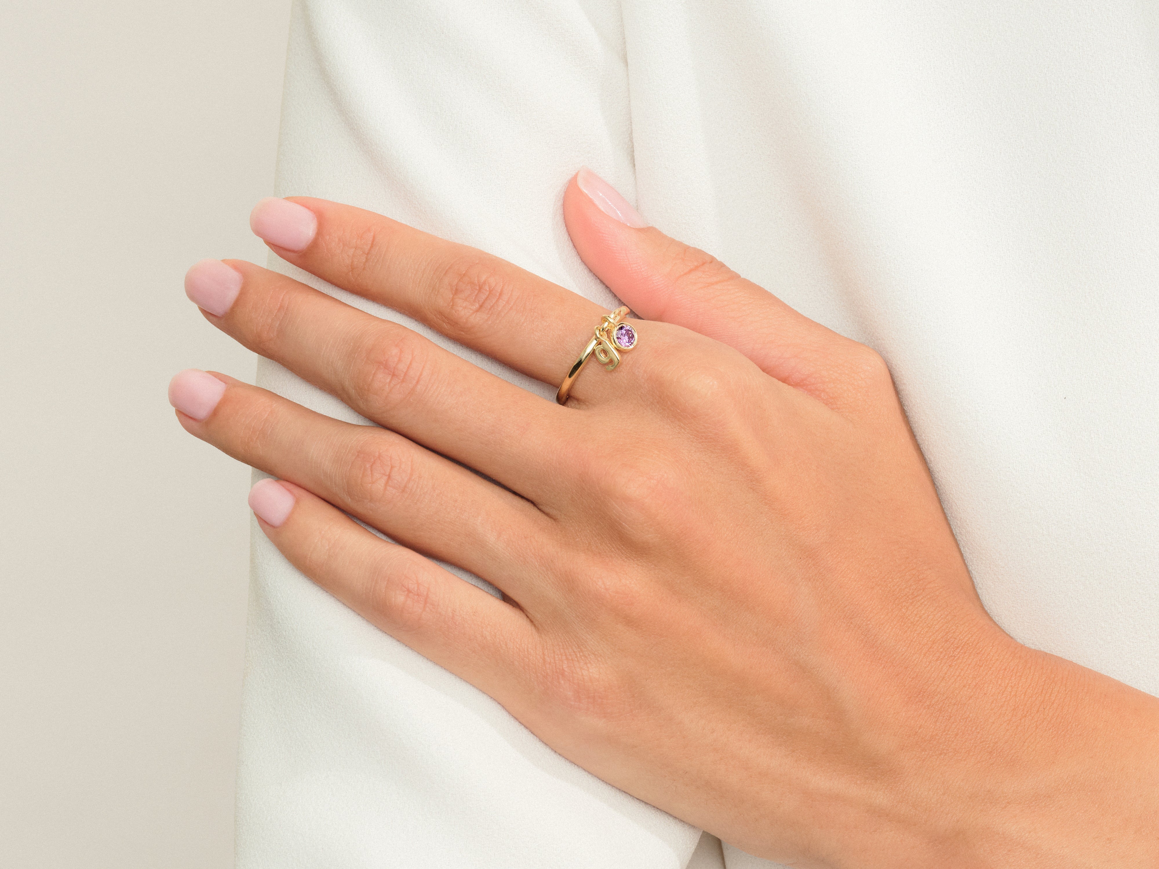 Gold ring with purple gemstone and charm on hand