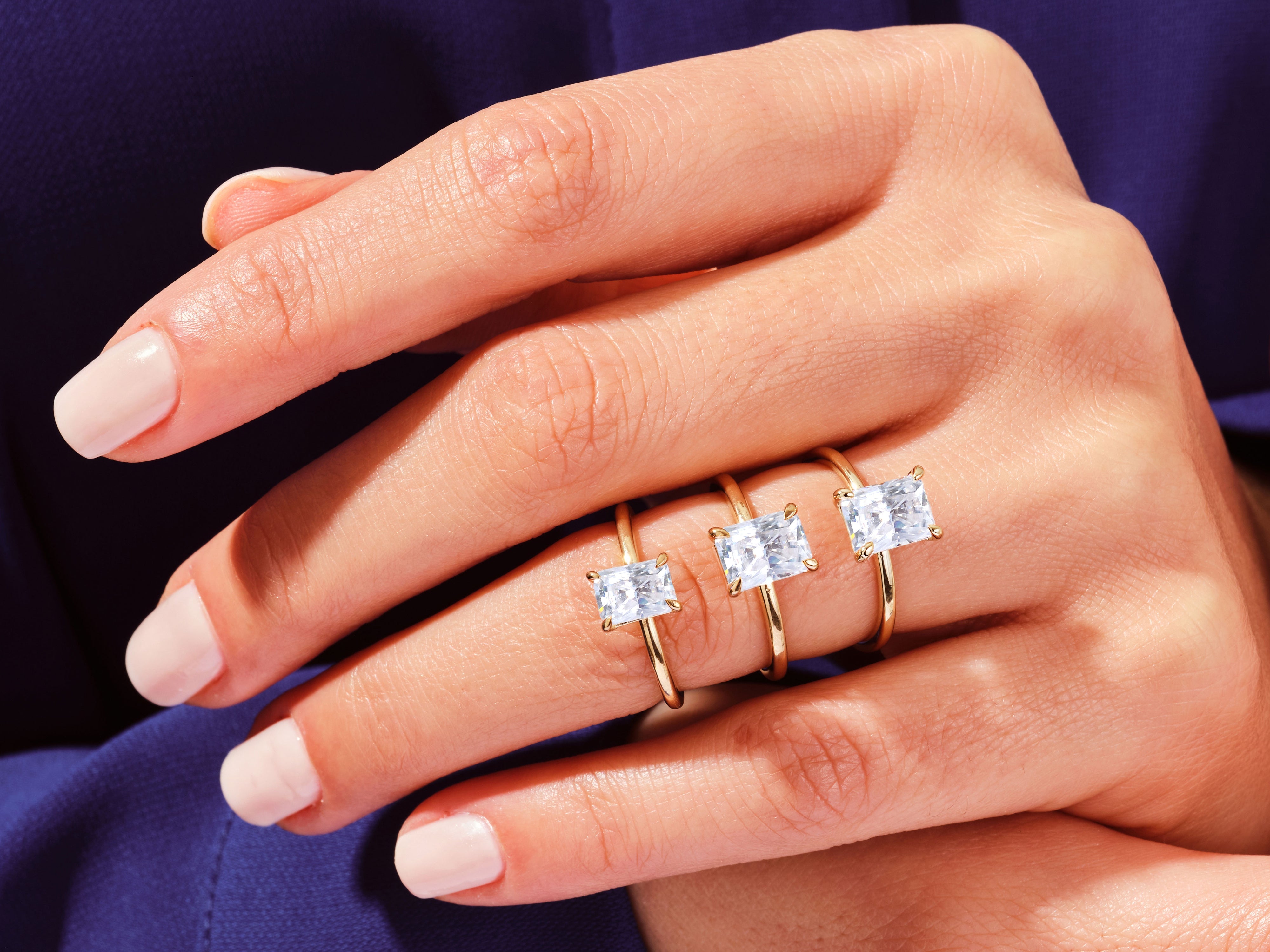 Three gold rings with emerald-cut diamonds on a hand