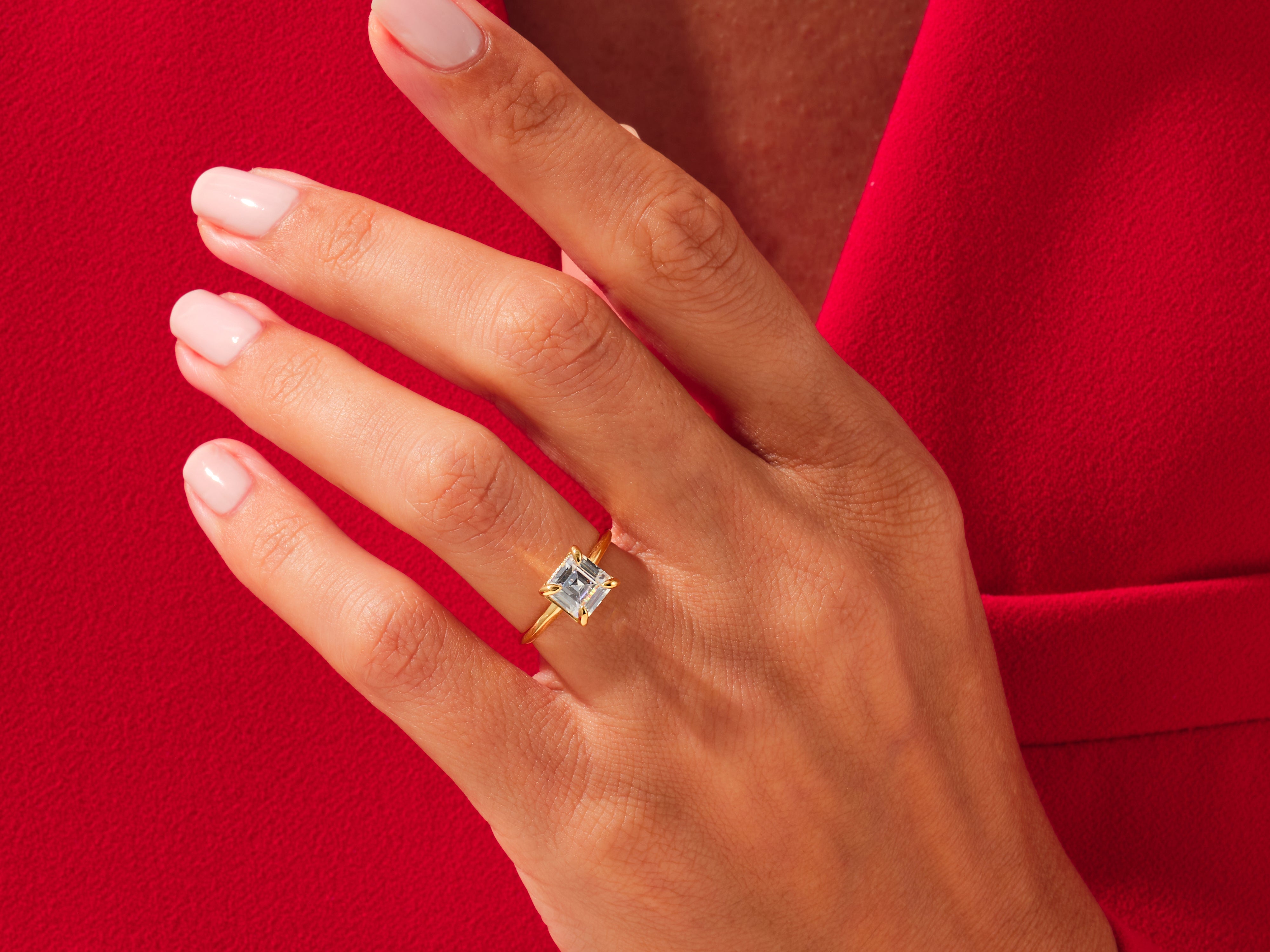 Gold ring with square diamond on hand, red background