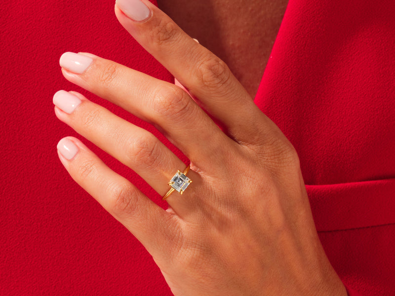 Gold ring with square diamond on hand, red background