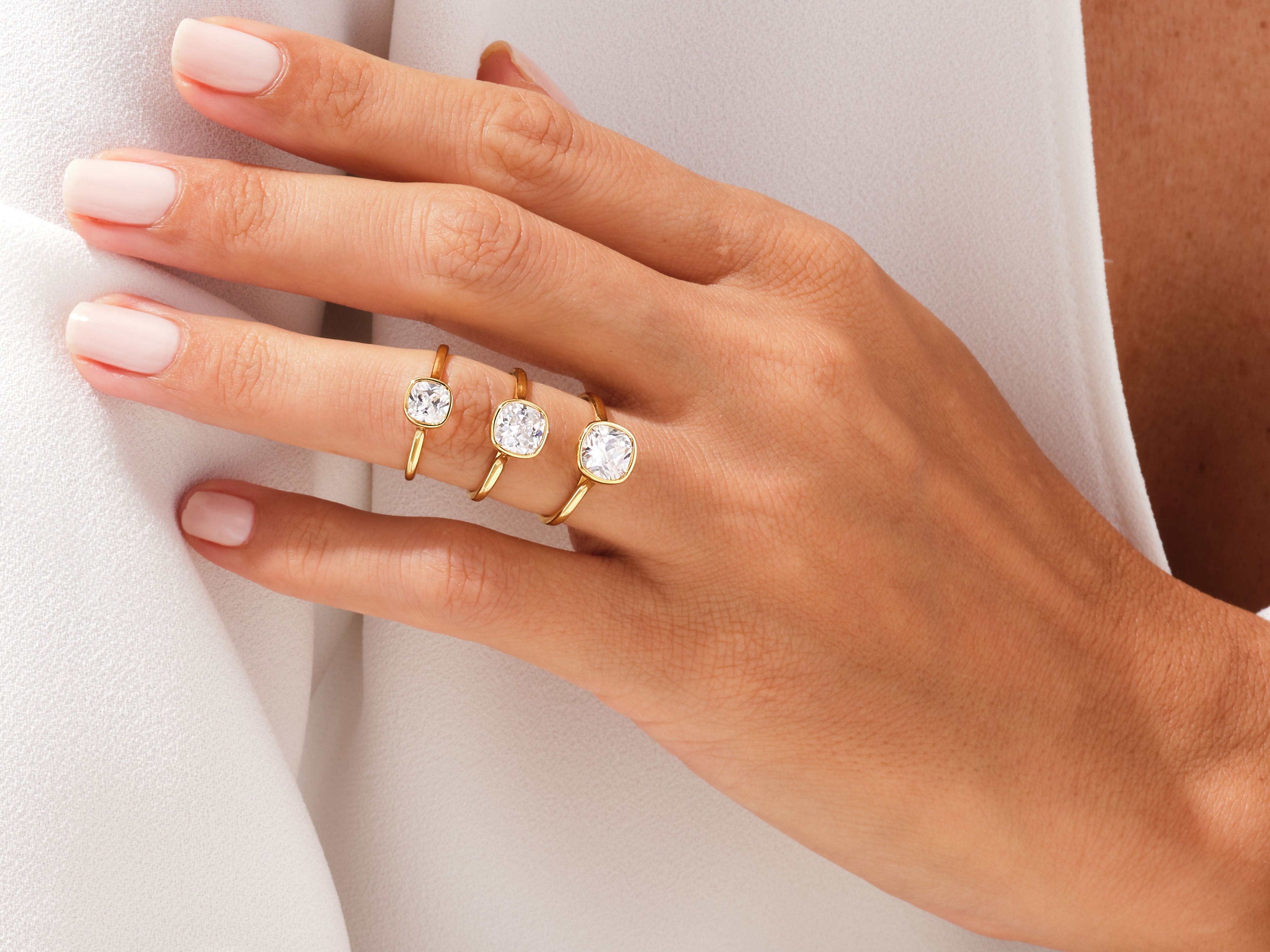 Gold rings with cushion-cut diamonds on a hand