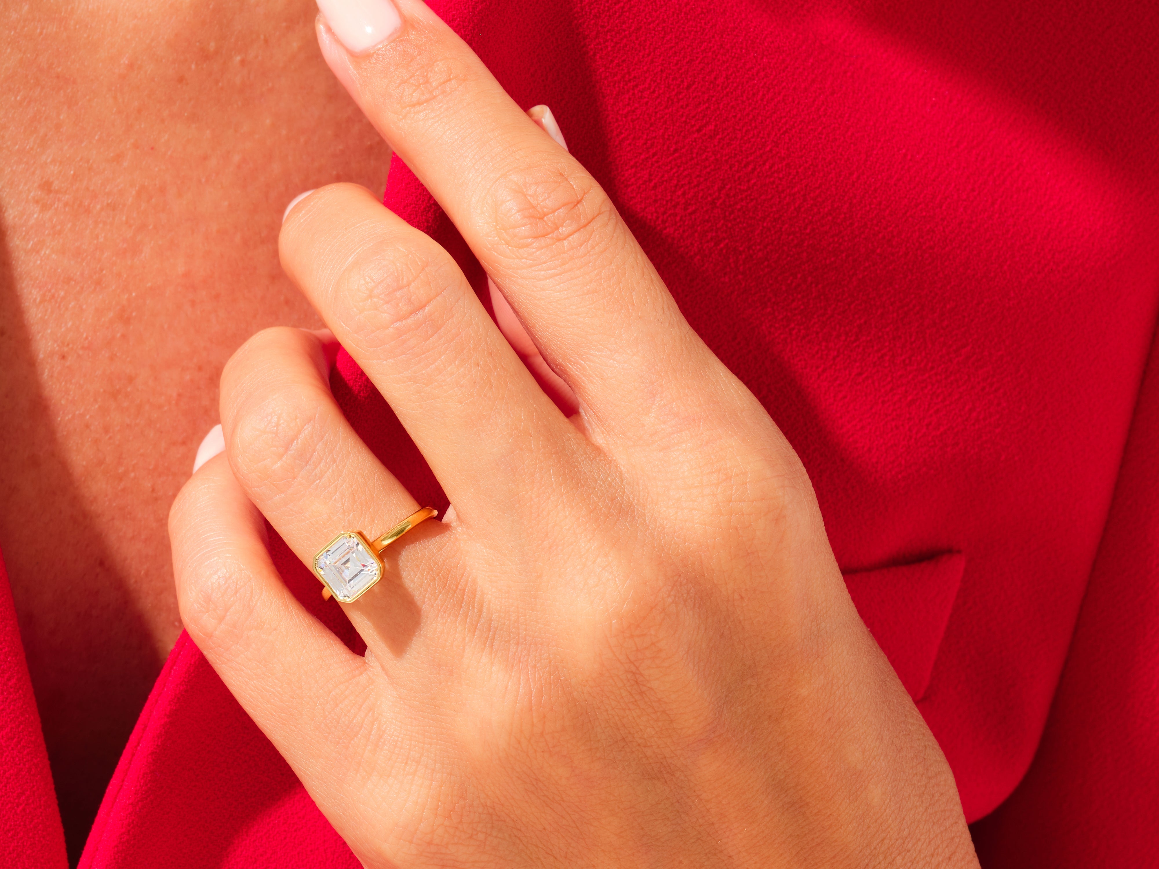 Emerald cut diamond ring on a hand, red blazer background