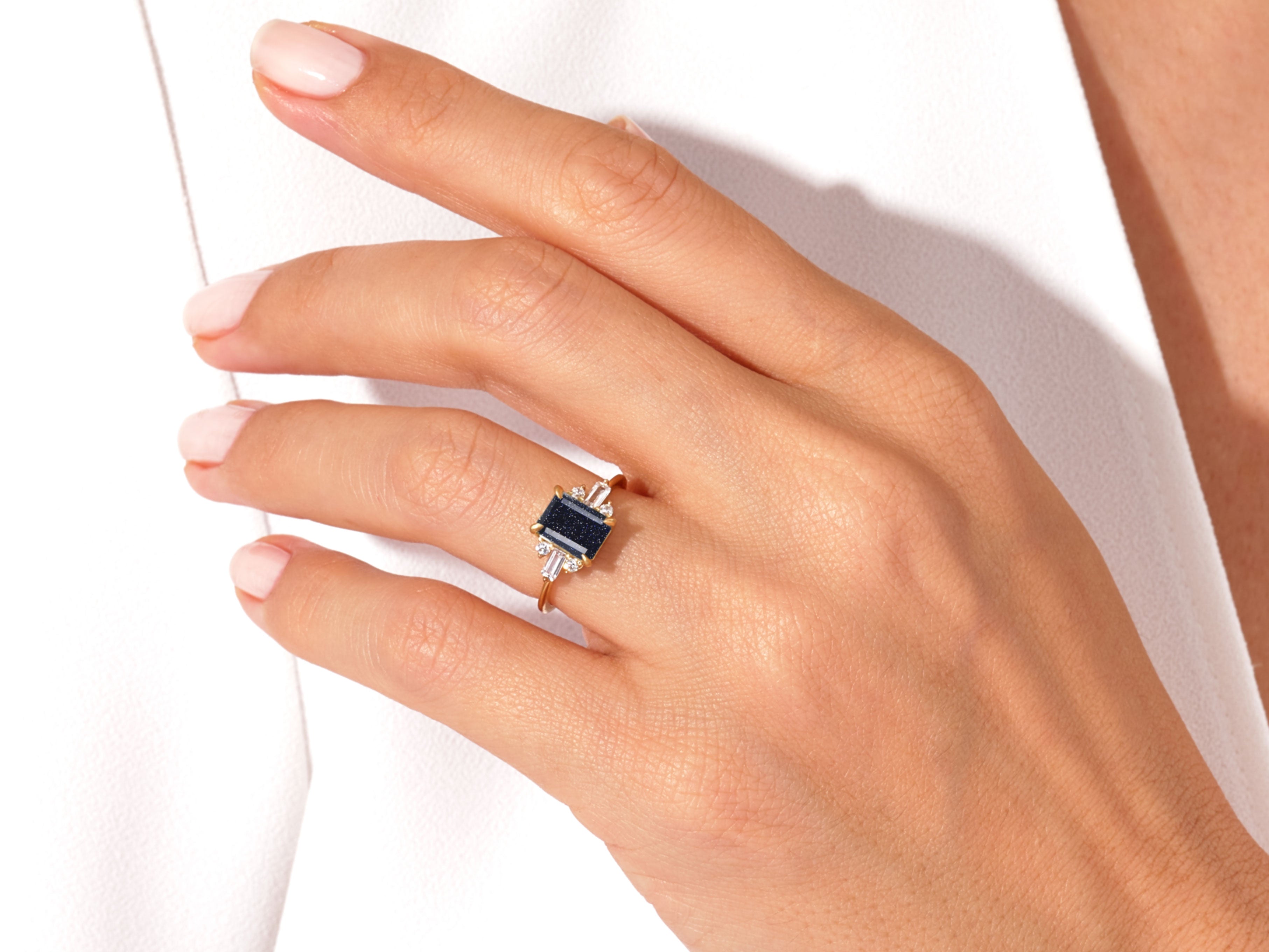 Emerald cut blue stone ring with diamond accents on a finger