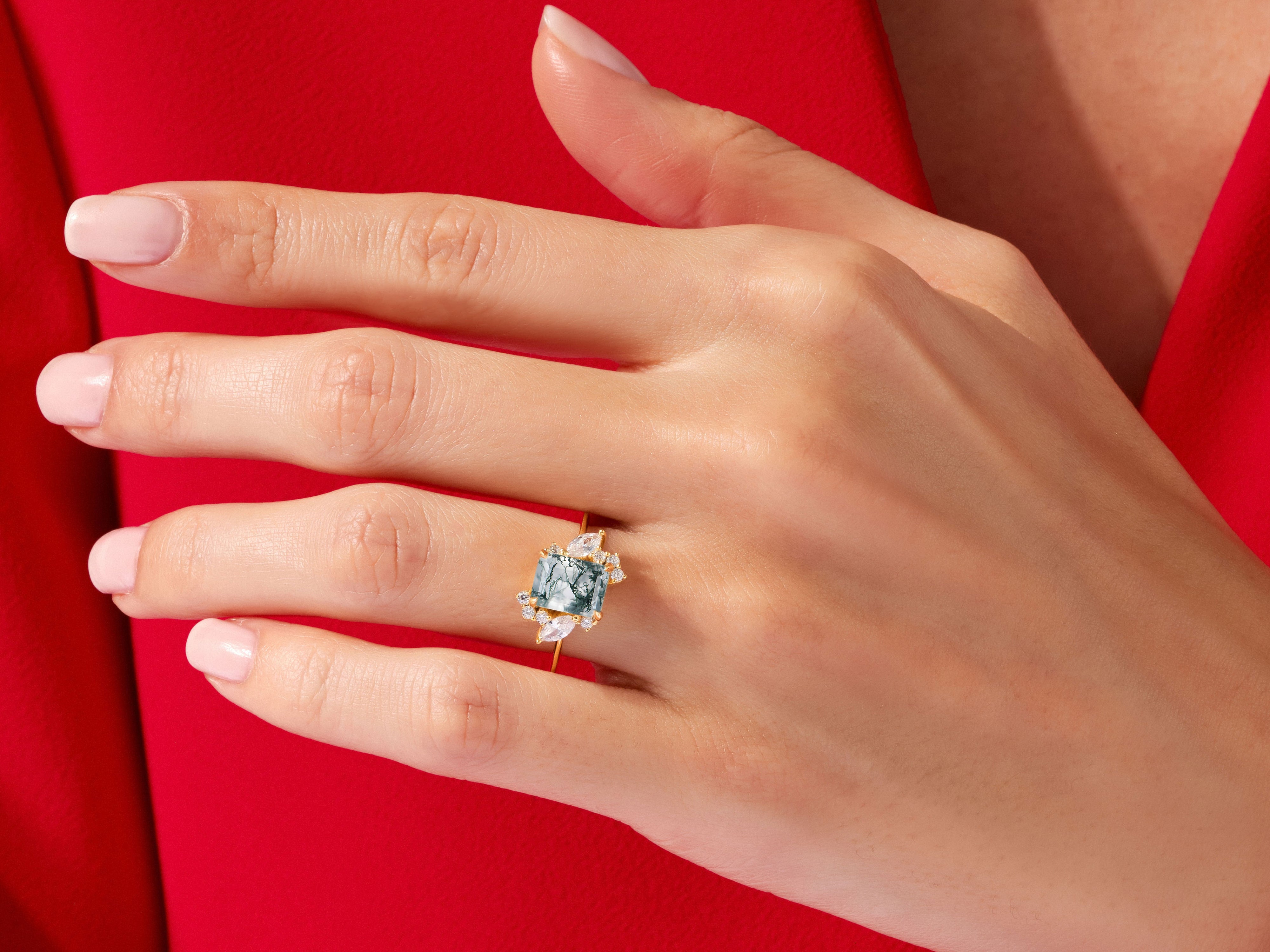 Emerald cut moss agate ring with diamond accents on a red background