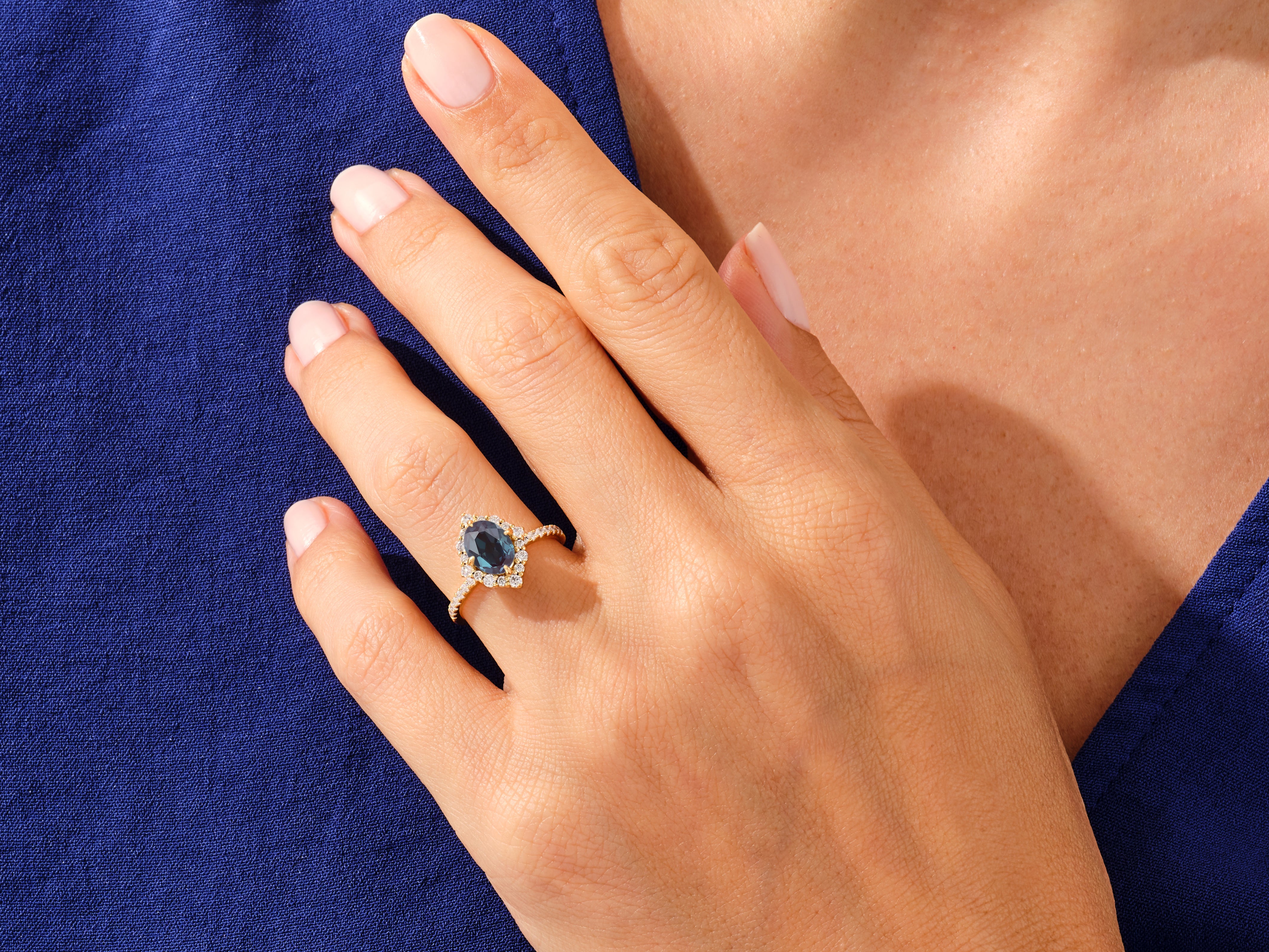Gold ring with oval blue gemstone and diamonds on hand
