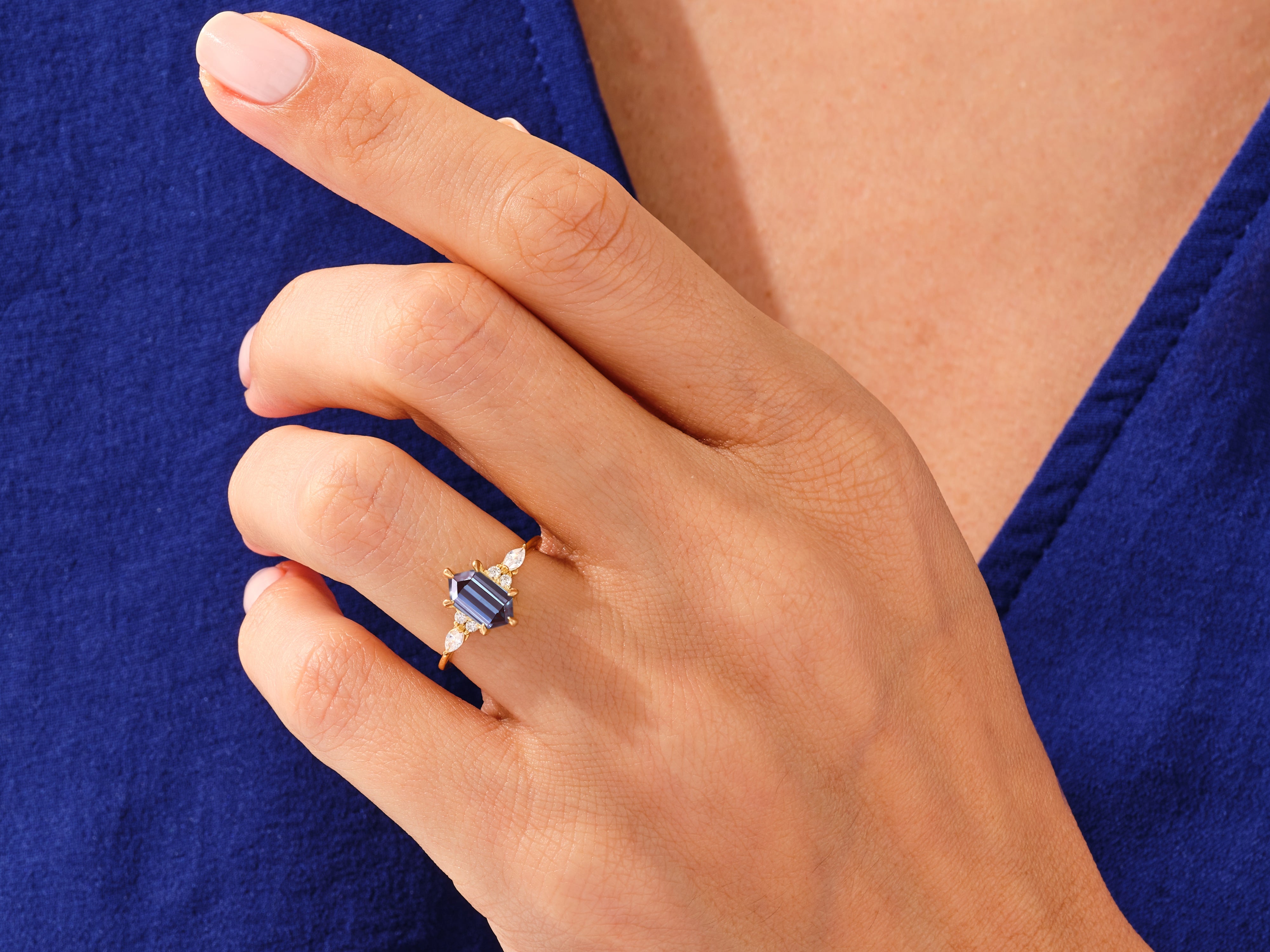 Emerald cut sapphire ring with diamond accents on a hand