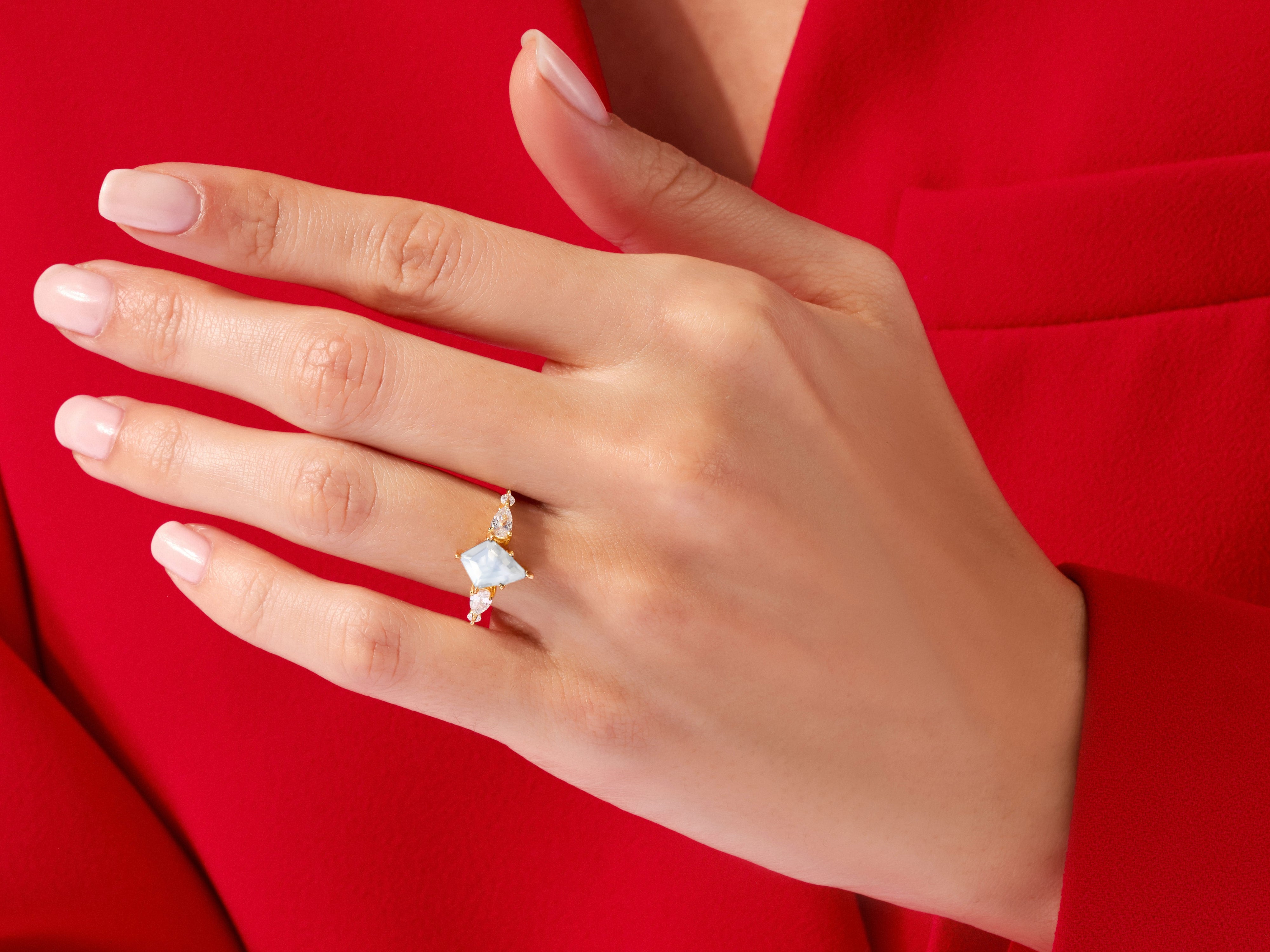 Gold ring with light blue gemstone and diamonds on a red background