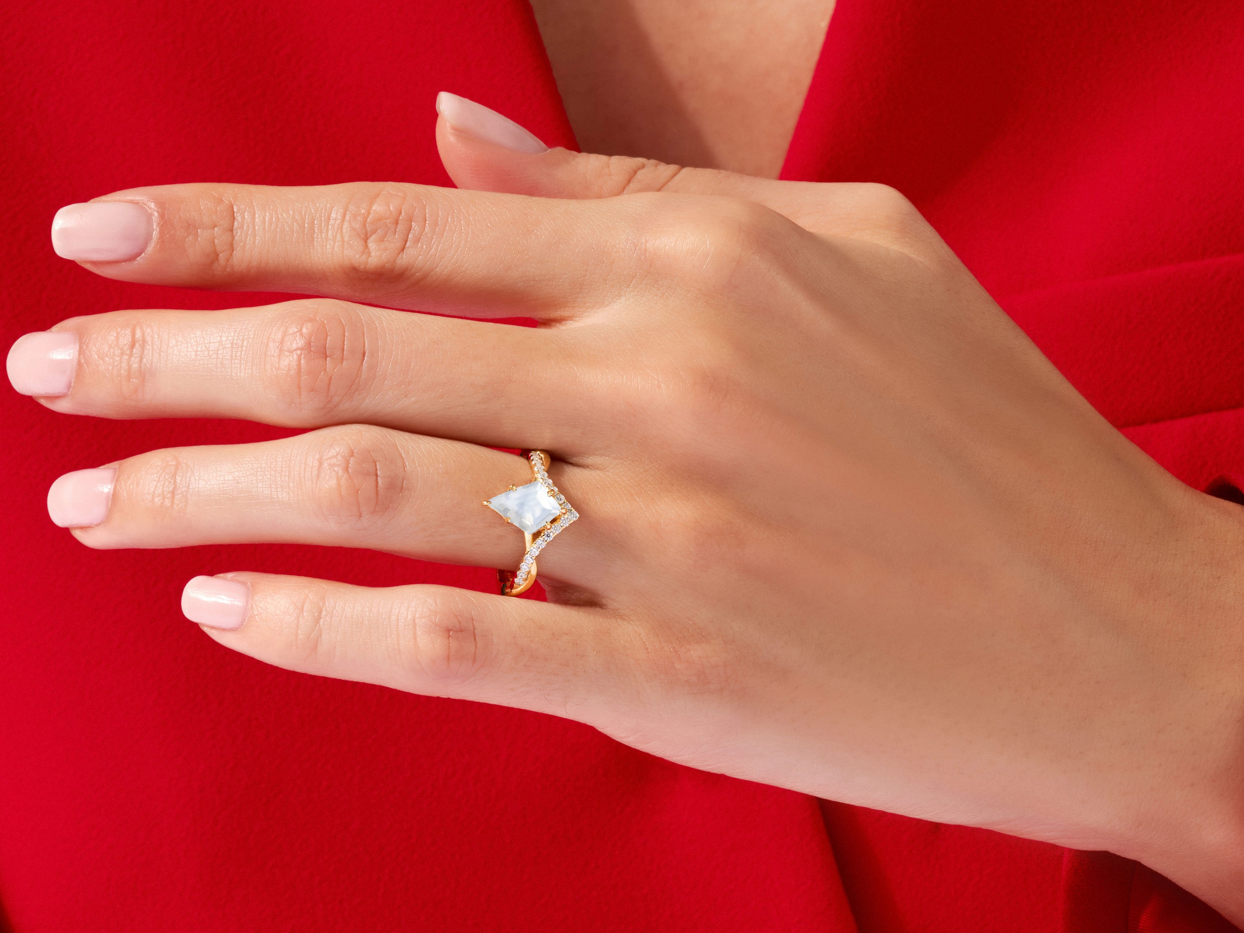 Gold ring with diamond accents and a pale blue gemstone on a red background