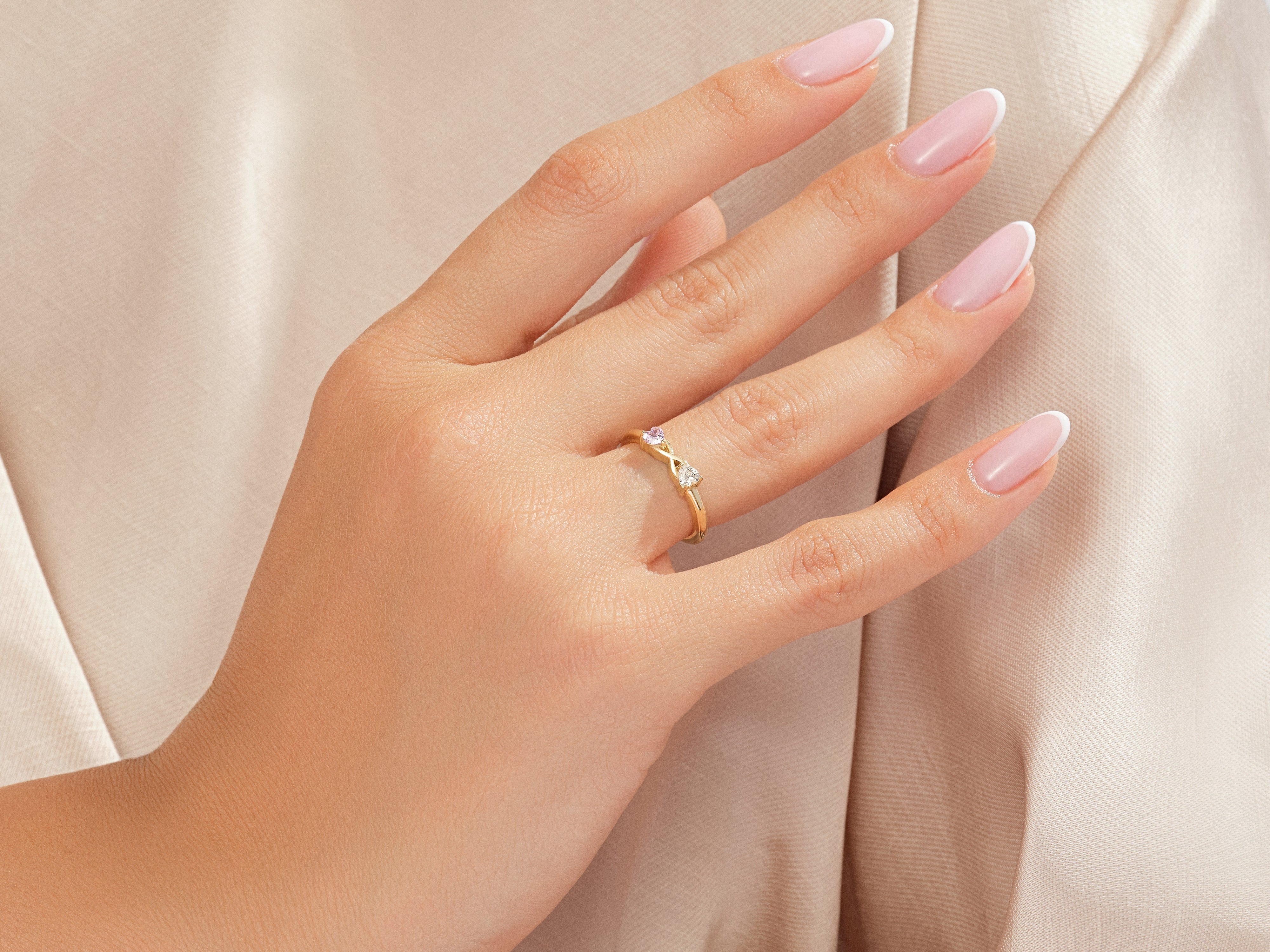 Gold infinity ring with diamonds and pink sapphire on a manicured hand