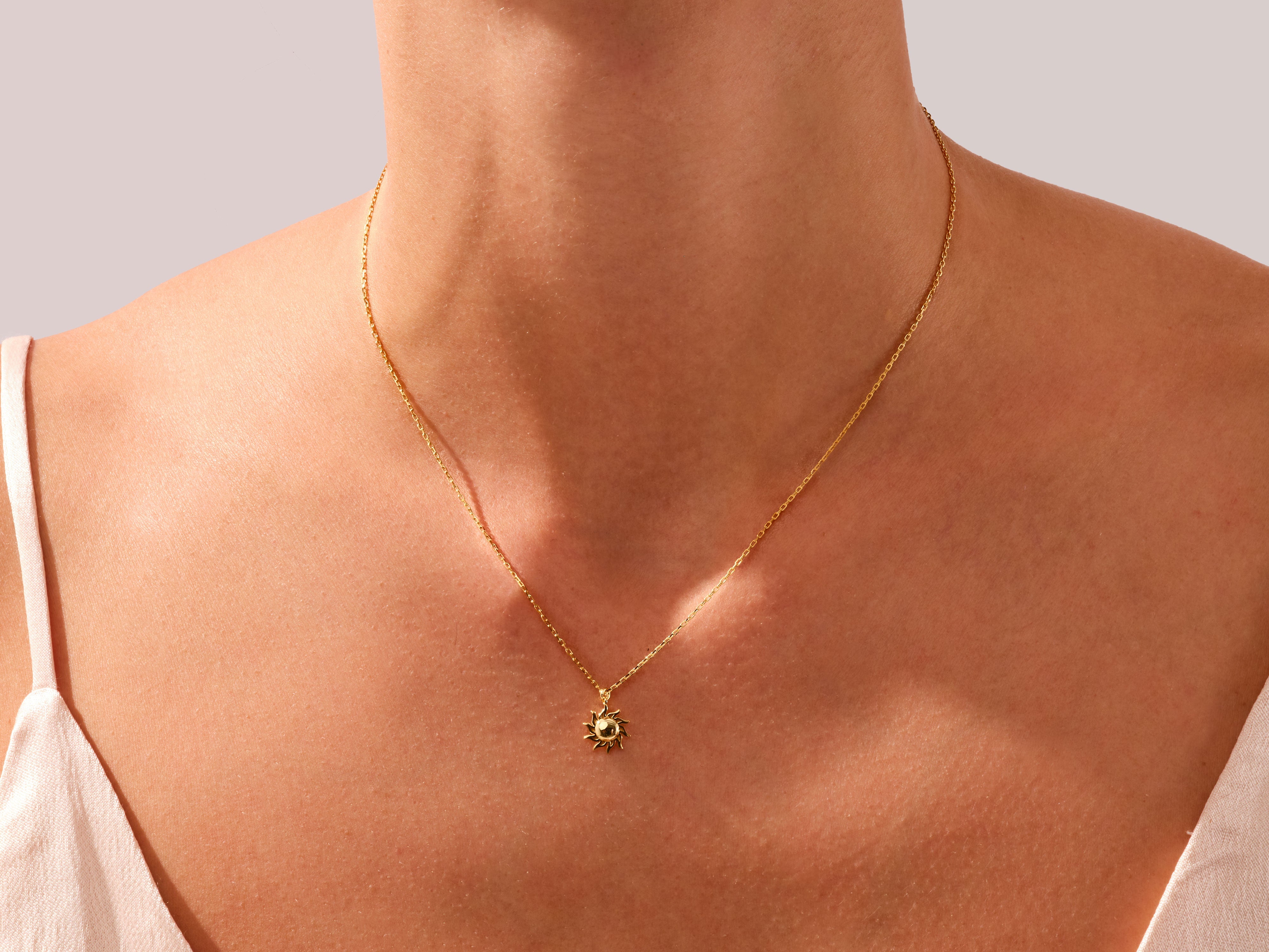 Gold sun pendant necklace on a woman's neck