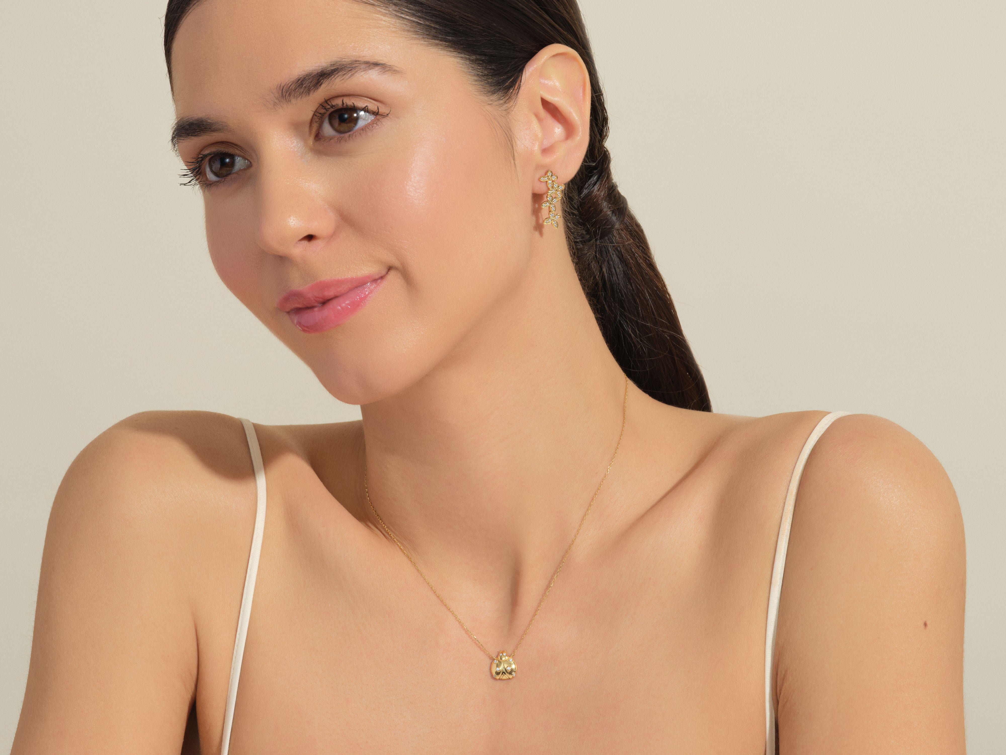 Model wearing gold diamond flower earrings and ladybug necklace