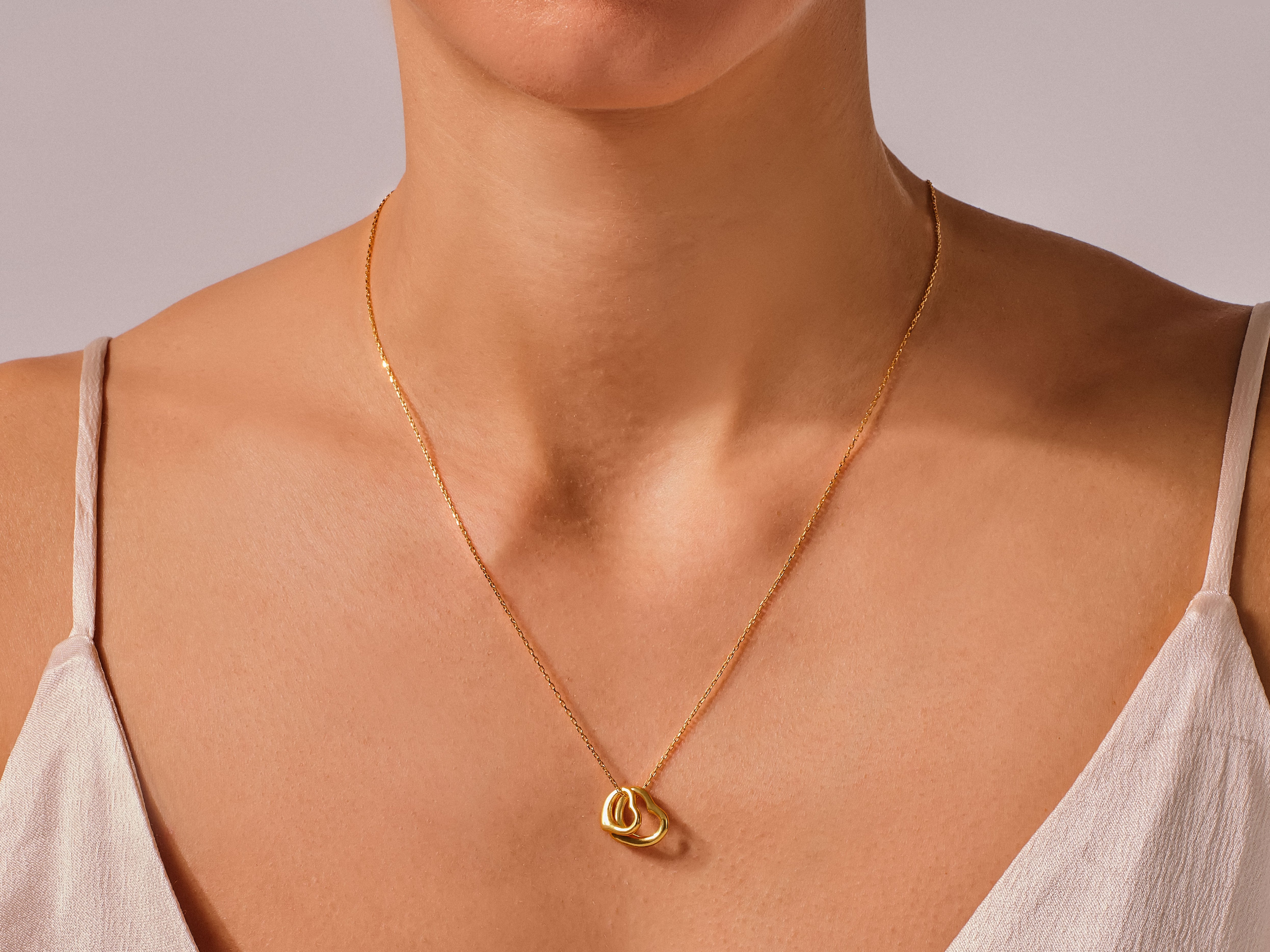 Gold interlocking heart necklace on a woman's neck