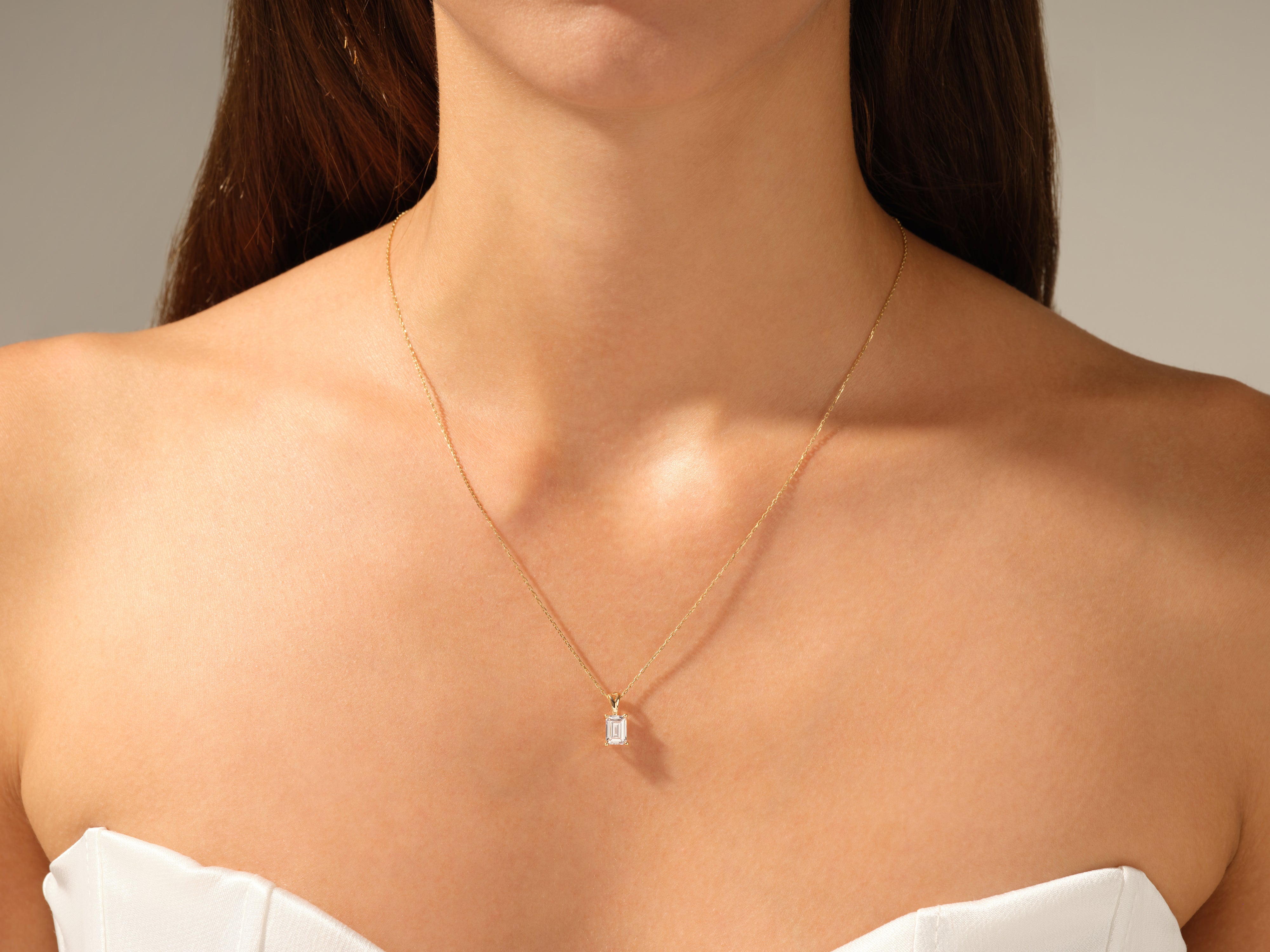 Gold necklace with emerald-cut diamond pendant on a woman's neck