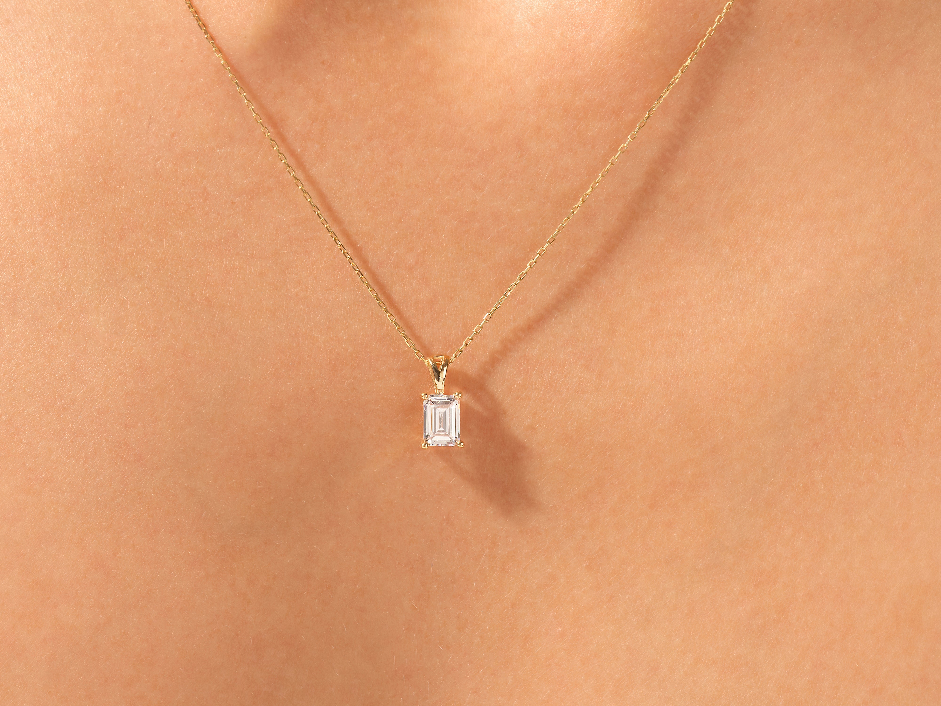 Gold necklace with emerald cut diamond pendant on skin