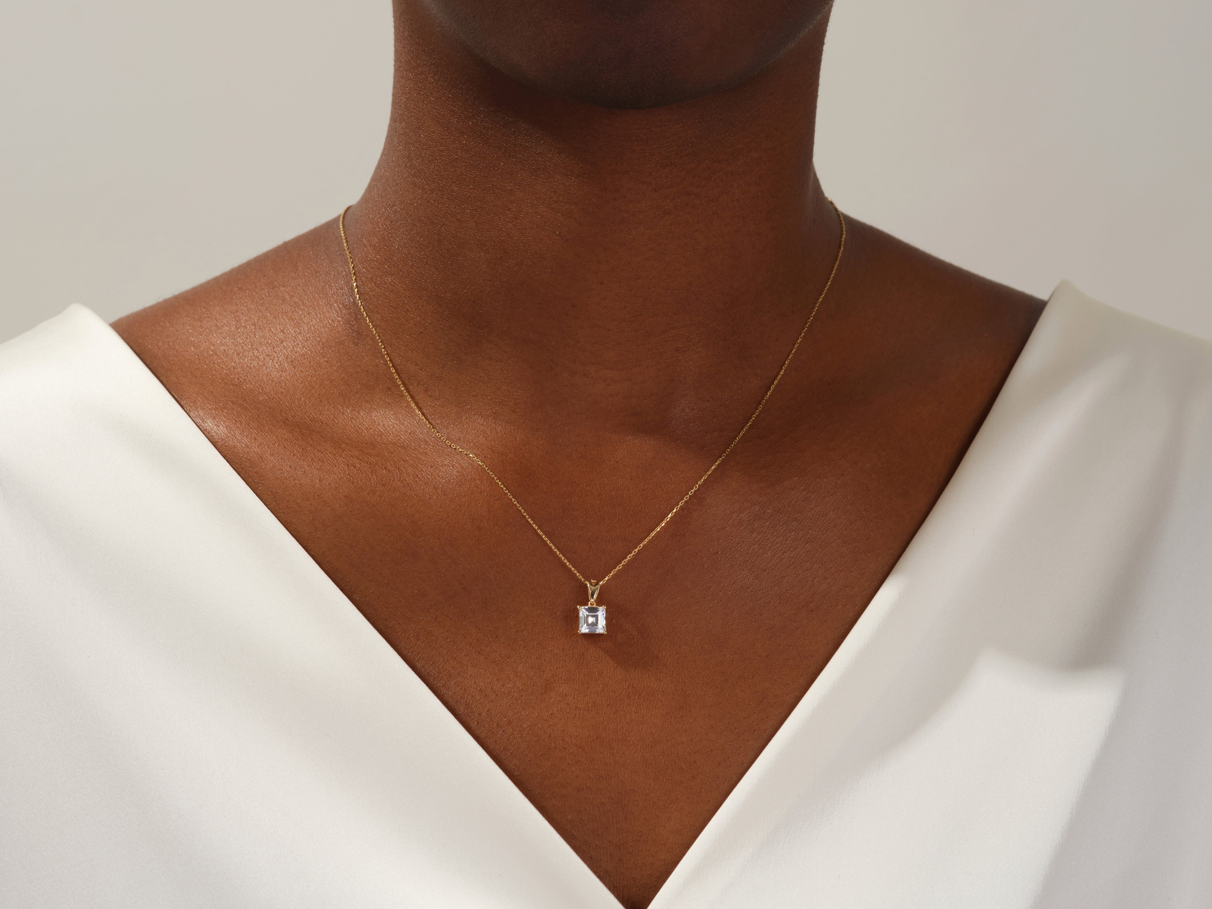 Gold necklace with emerald-cut diamond pendant on a woman's neck