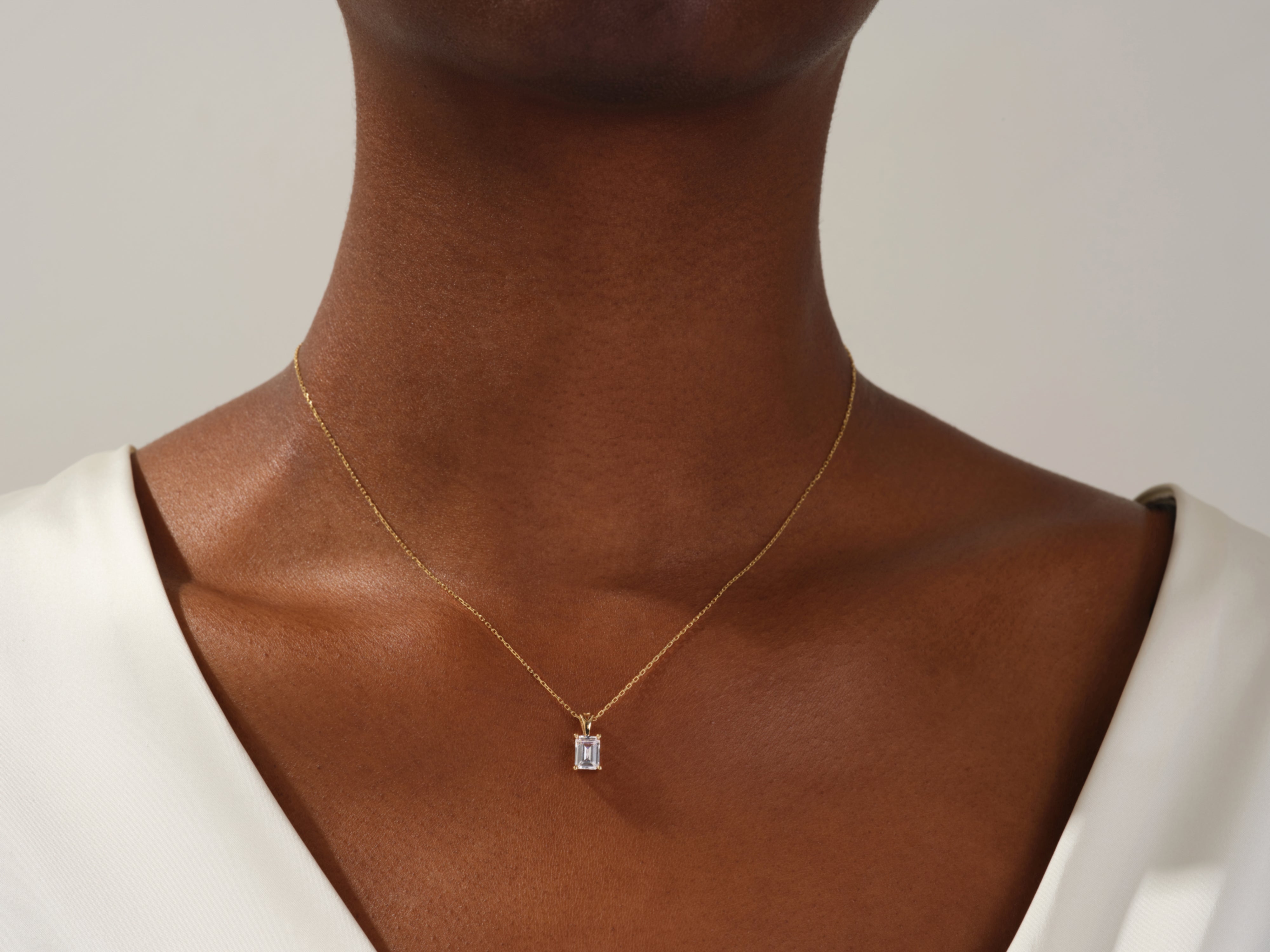 Gold necklace with emerald-cut diamond pendant on a woman's neck