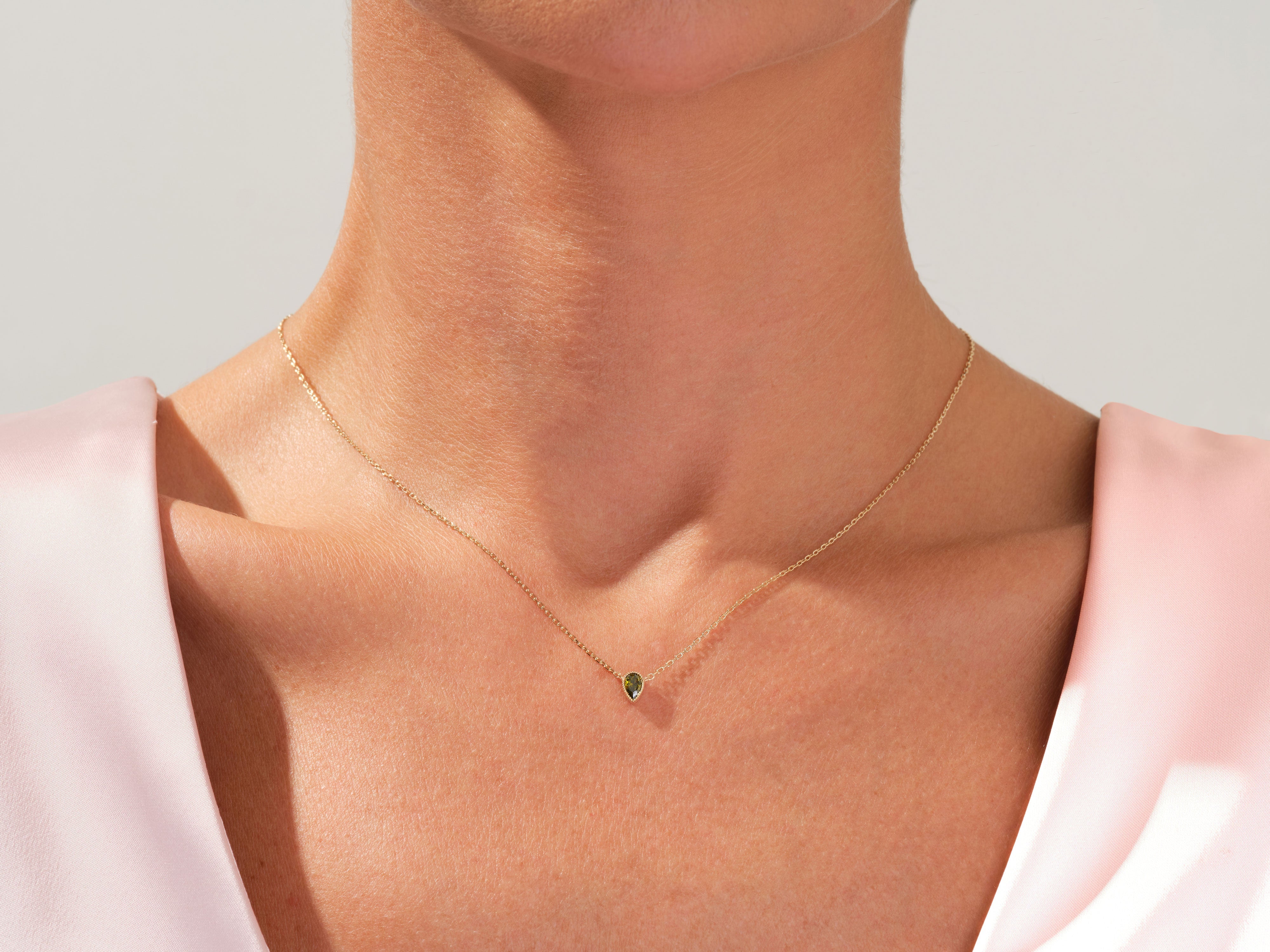 Gold necklace with green gemstone pendant on a woman's neck