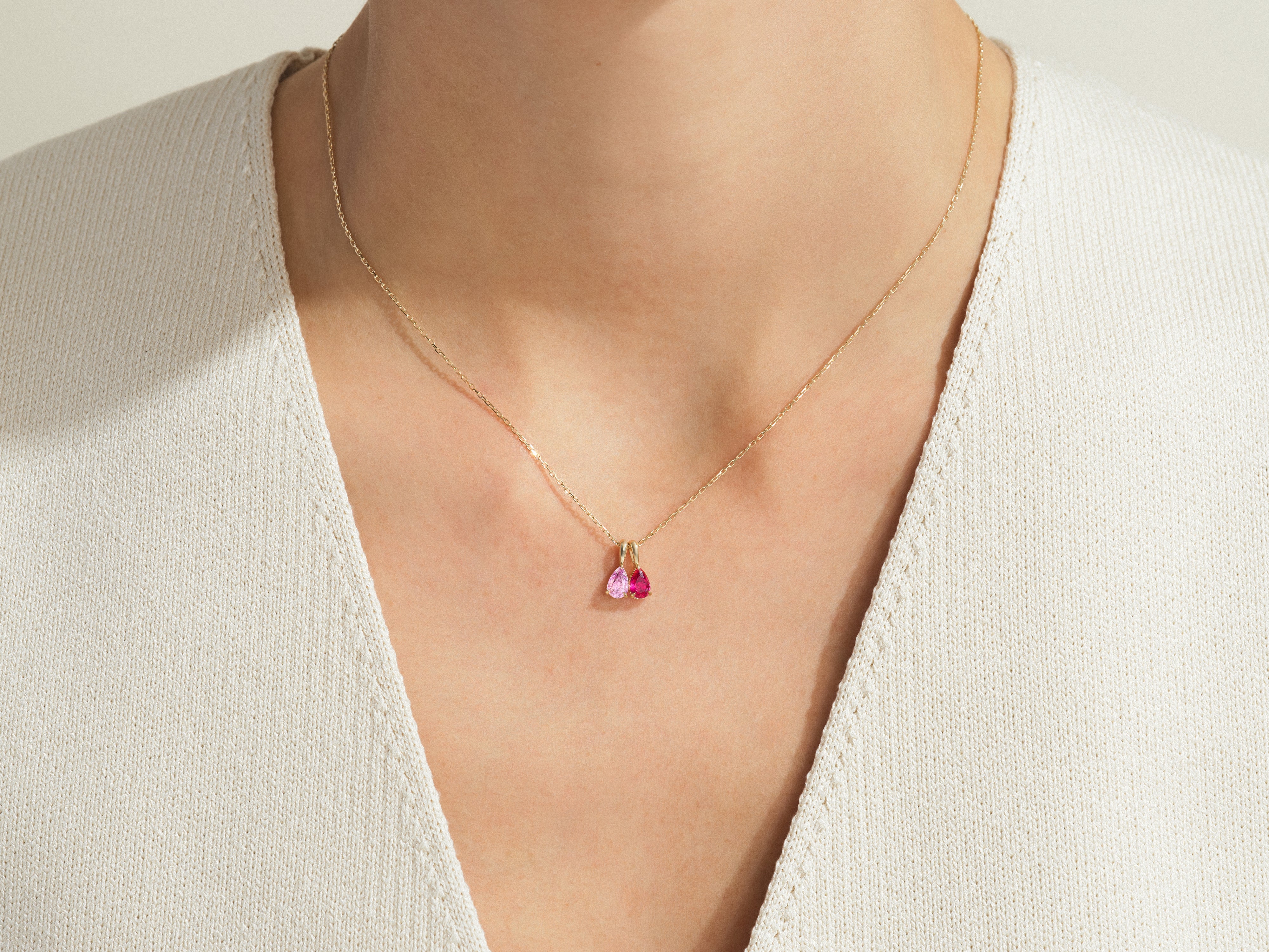 Gold necklace with pink and red gemstone pendants on a woman's neck