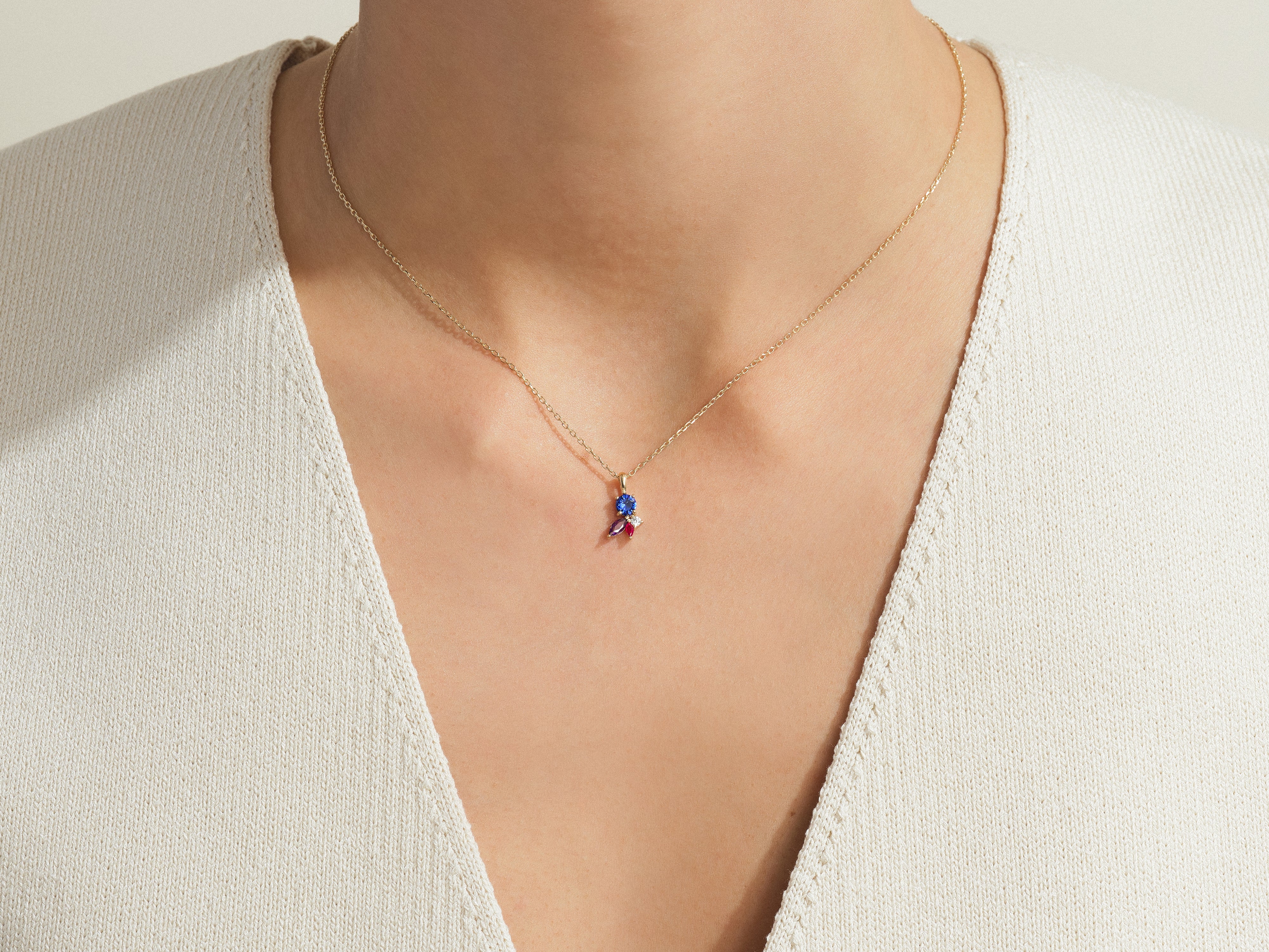 Gold necklace with blue and red gemstone pendant on a woman's neck
