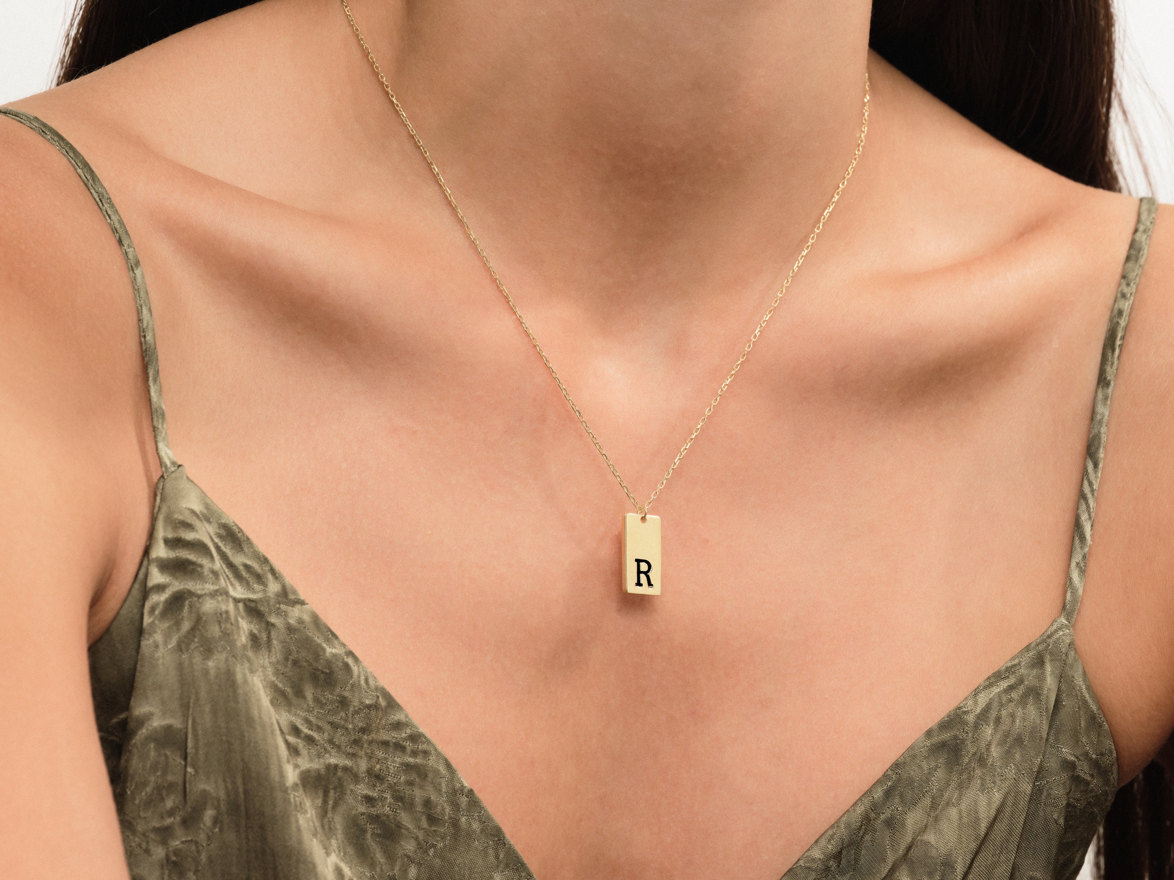 Gold initial necklace 'R' on a woman's décolletage
