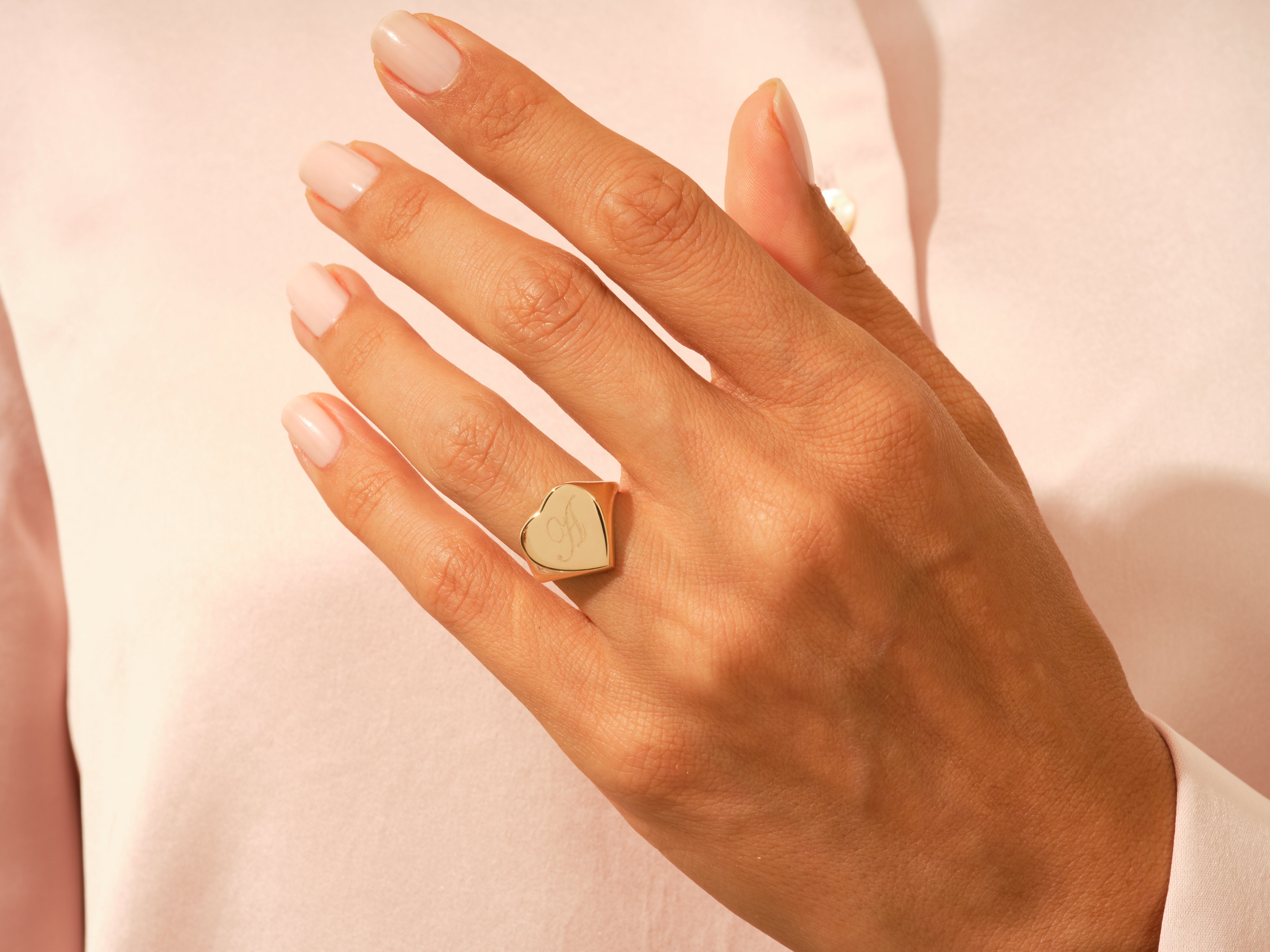Gold heart signet ring with initial 'A' on a hand