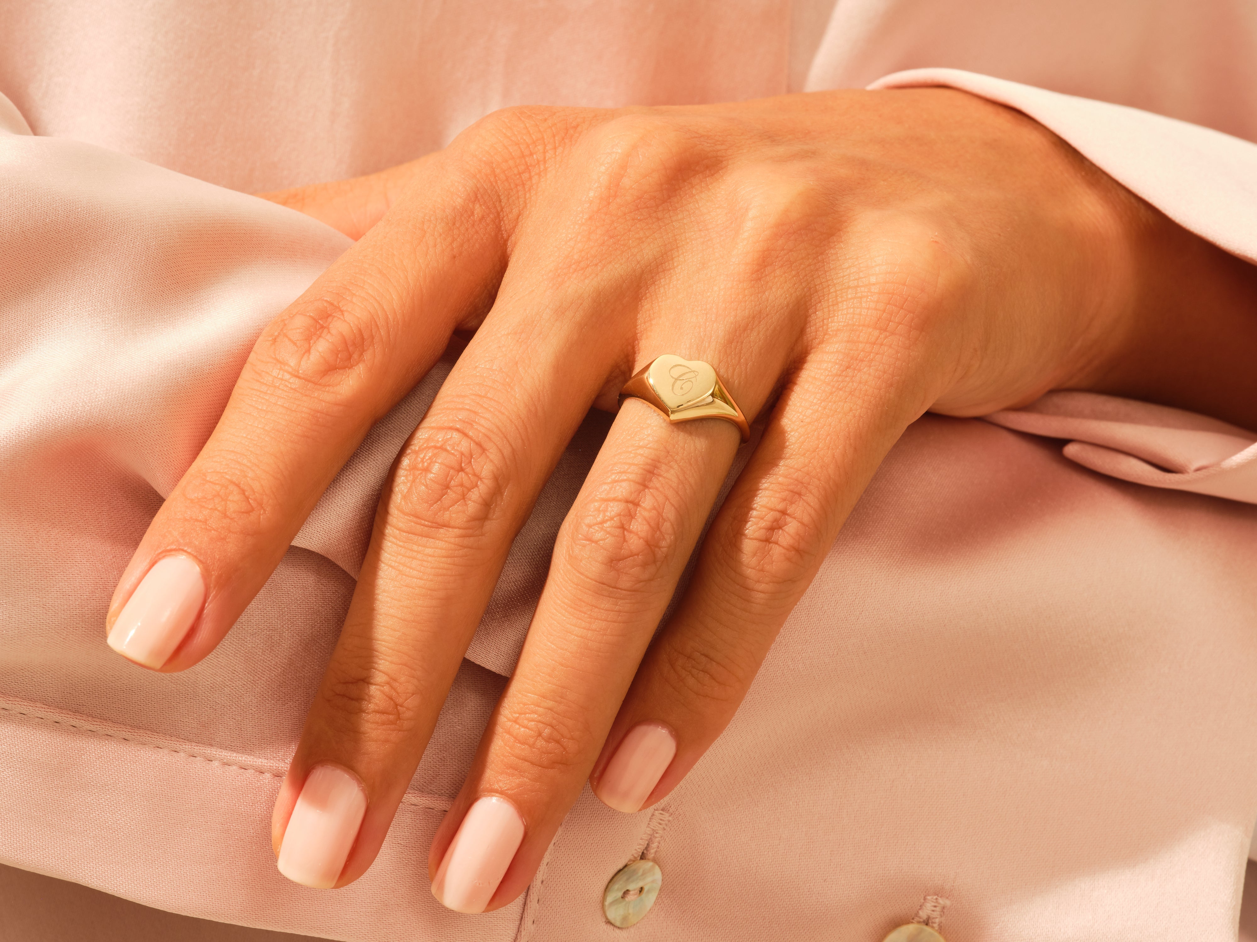 Gold heart signet ring with initial 'C' on a woman's hand