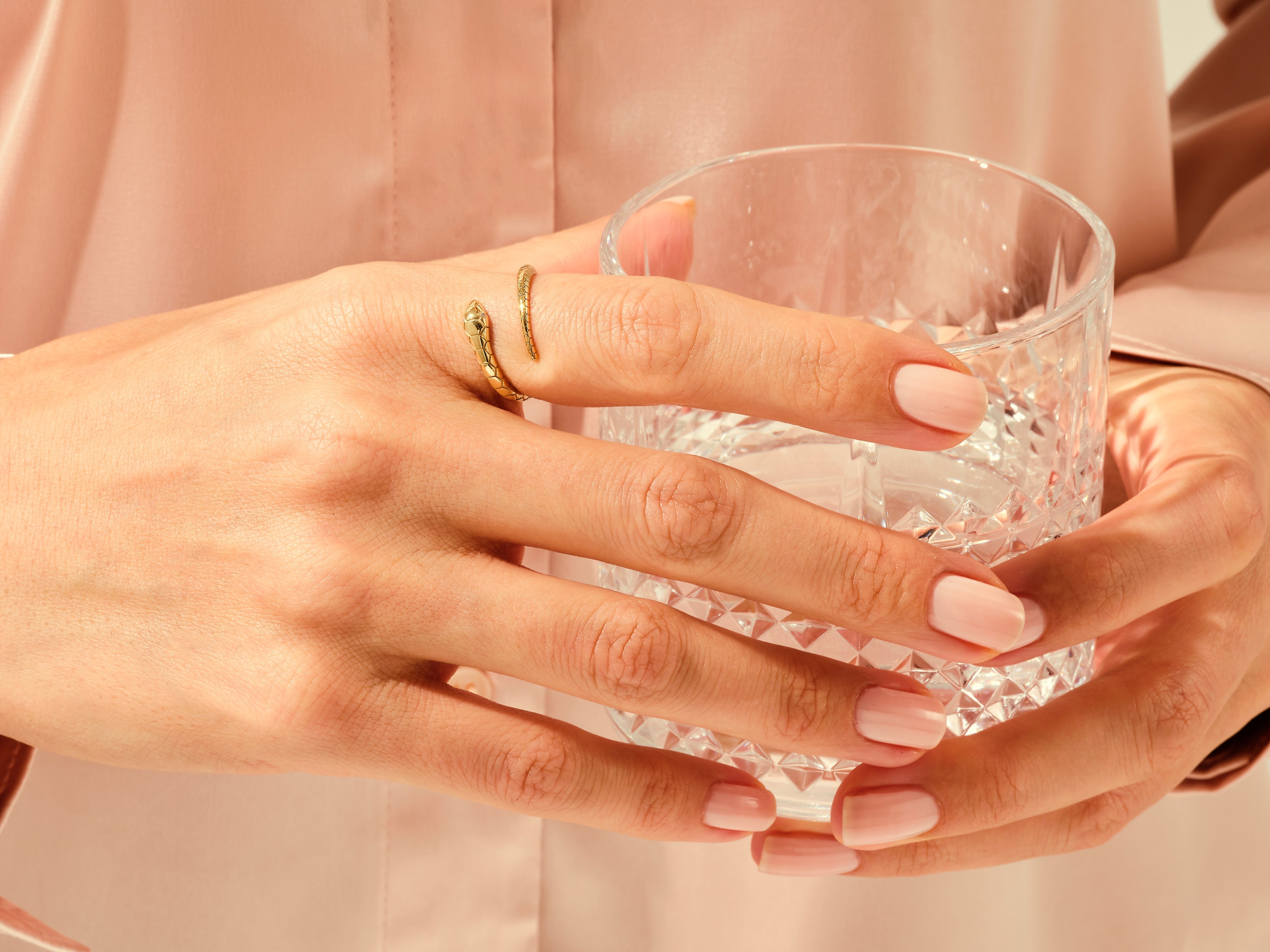 Gold snake ring on hand holding a crystal glass