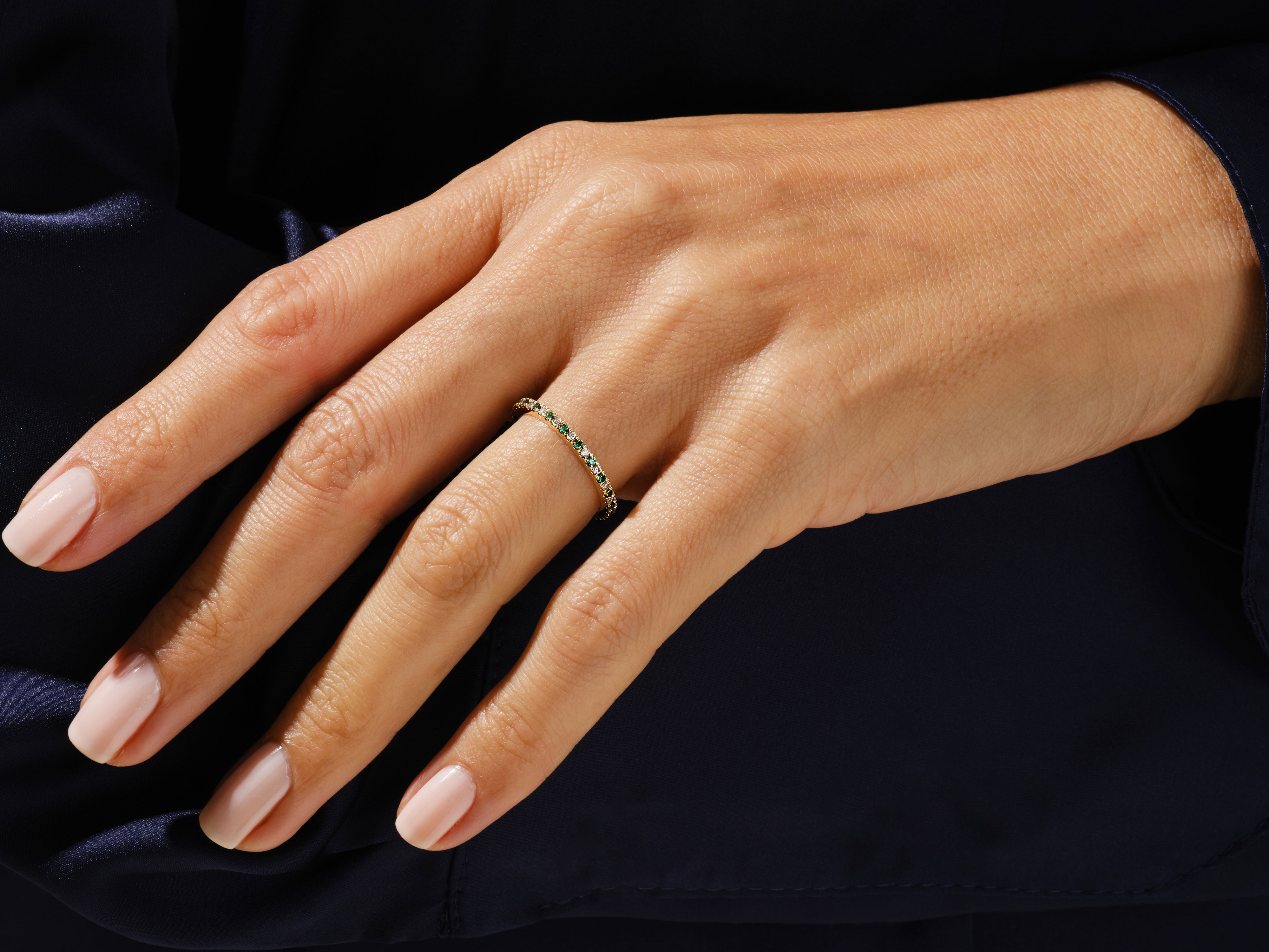 Gold eternity ring with emeralds and diamonds on a woman's hand