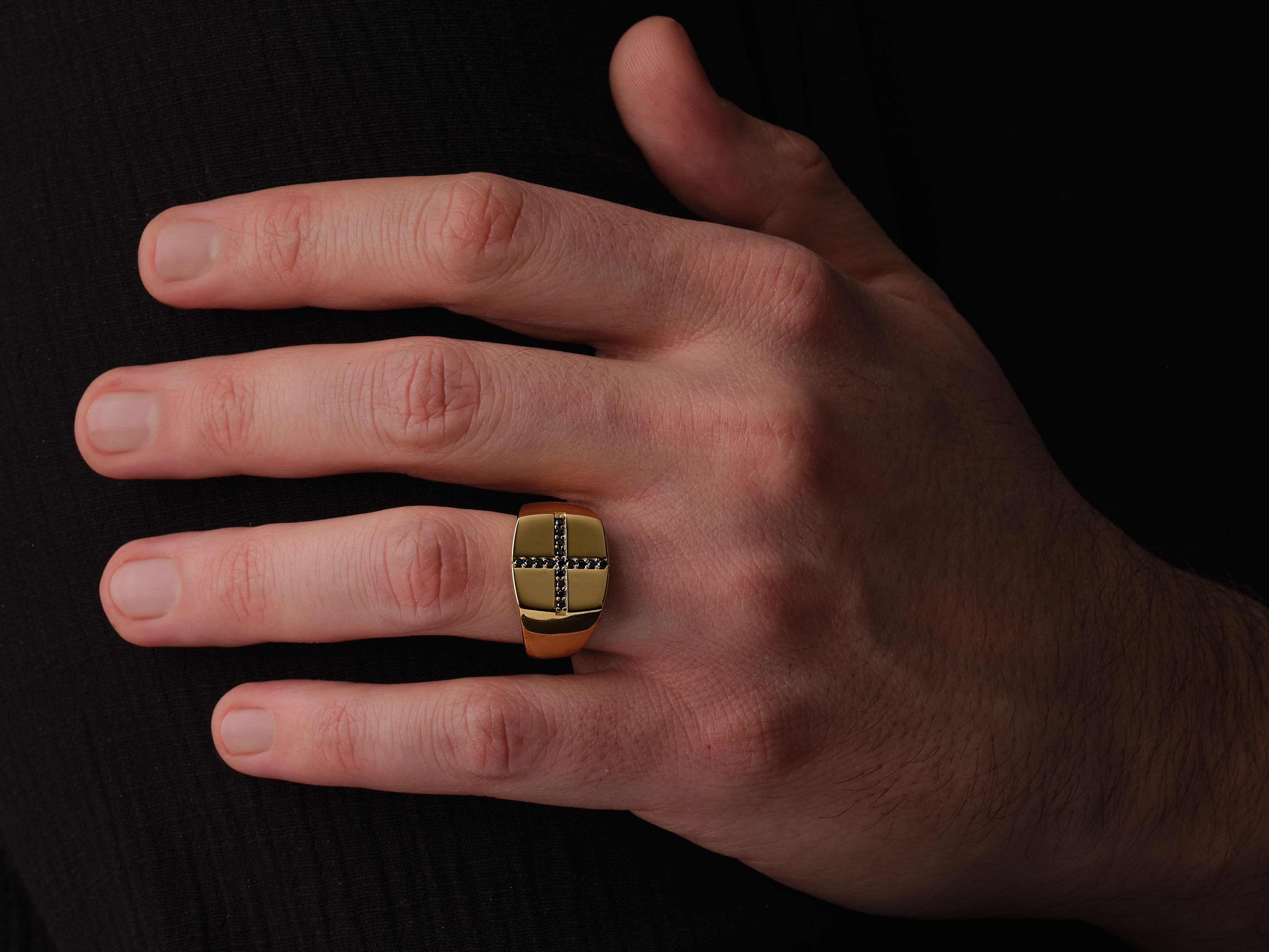 Gold ring with black diamond cross design on a man's finger