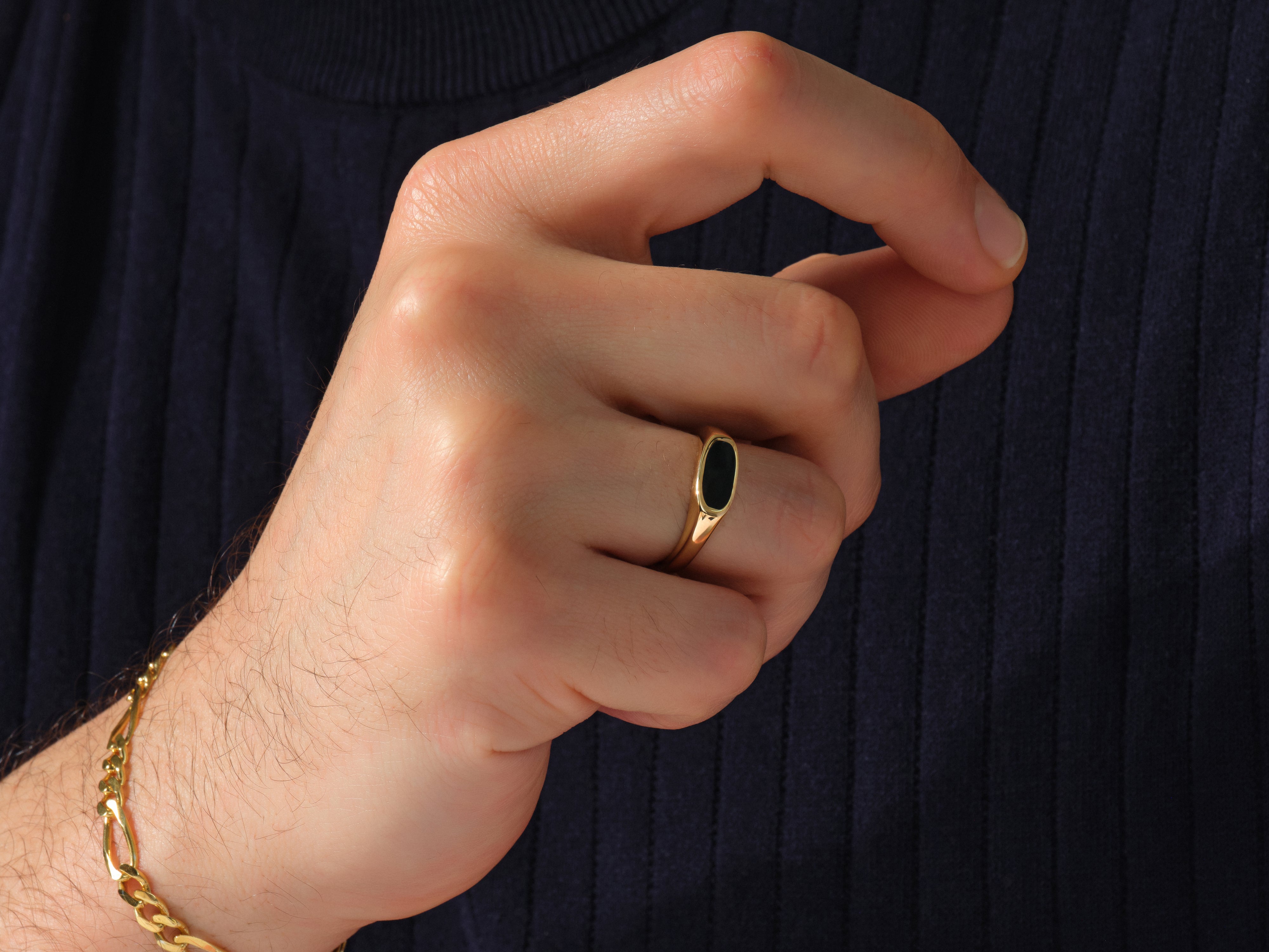 Gold signet ring with black stone and gold bracelet on hand