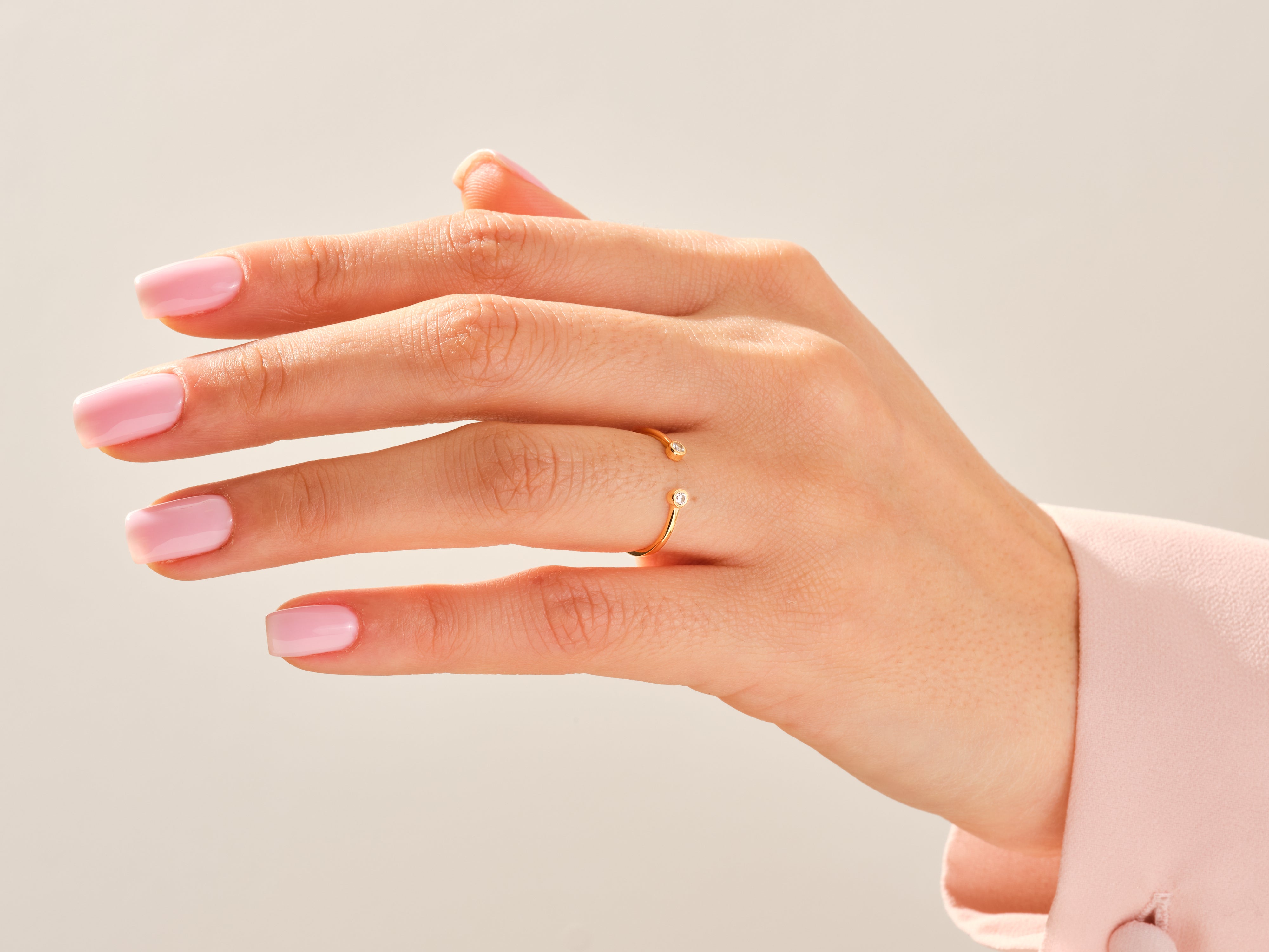 Gold diamond bypass ring on a hand with pink nails